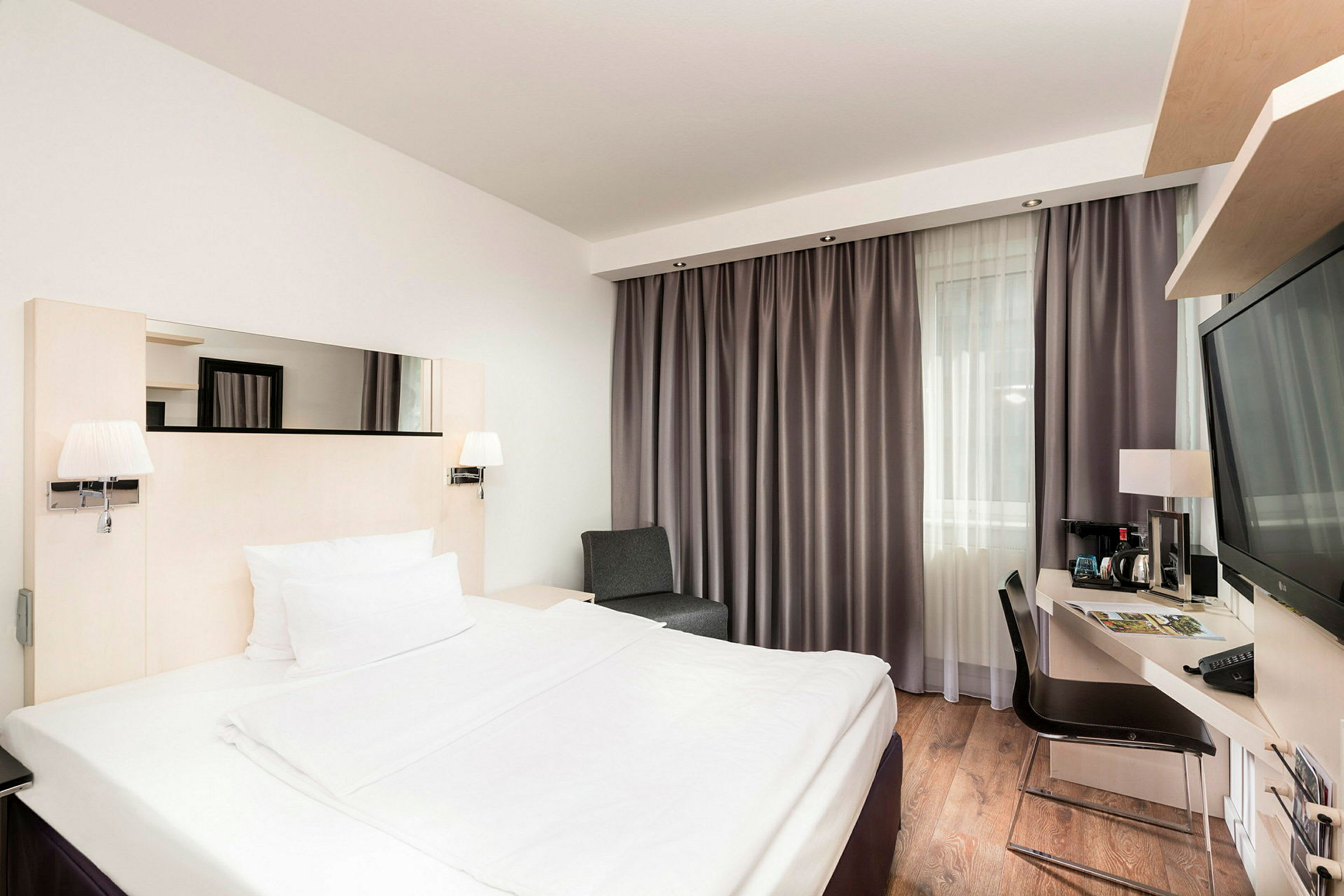 Hotellihuone, jossa on parivuode, kirjoituspöytä ja tuoli sekä suuri ikkuna verhoilla. (Tekoälyn luoma teksti)