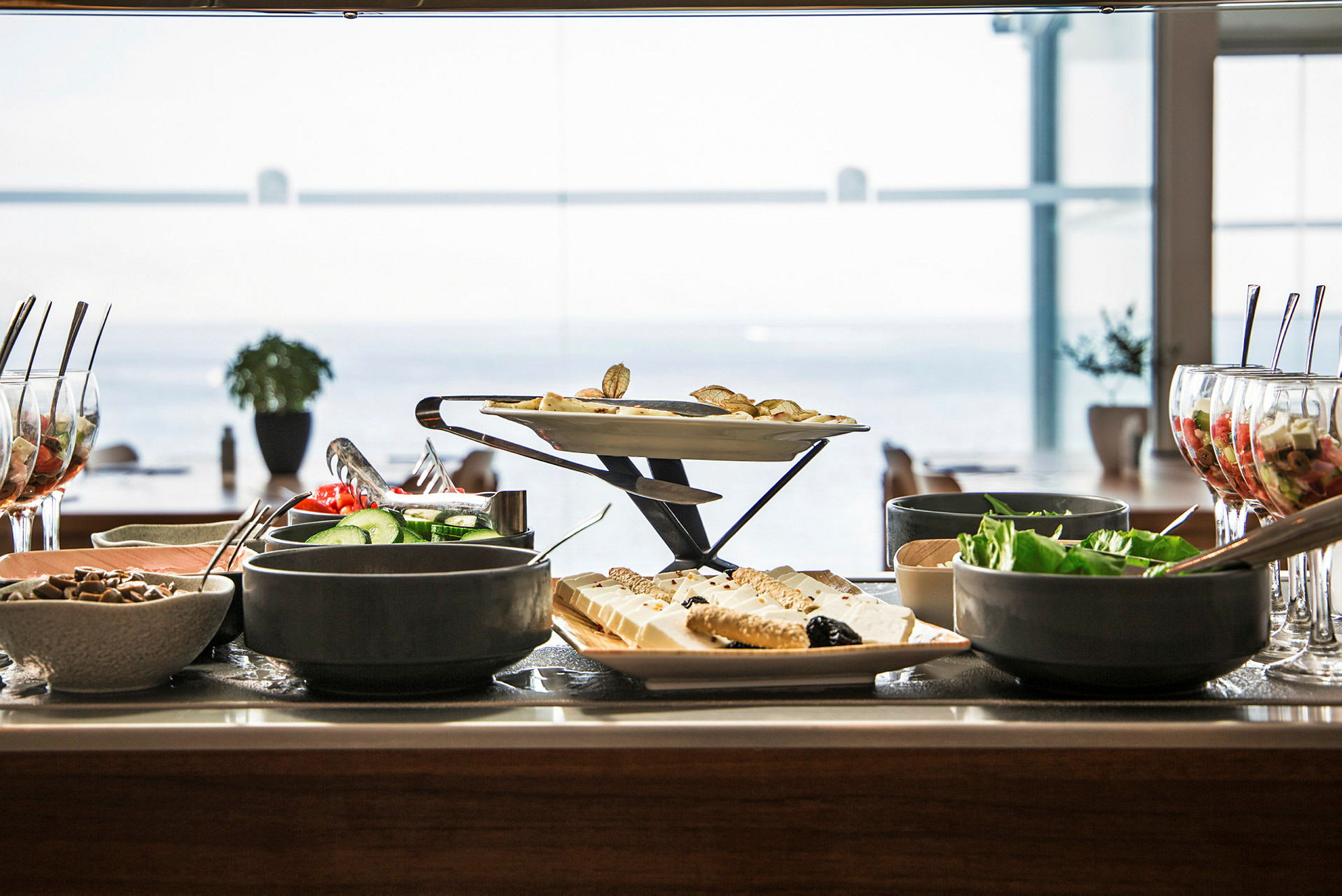 Buffet, jossa erilaisia ruokia, salaatteja ja jälkiruokia pöydällä, taustalla merinäkymä. (Tekoälyn luoma teksti)
