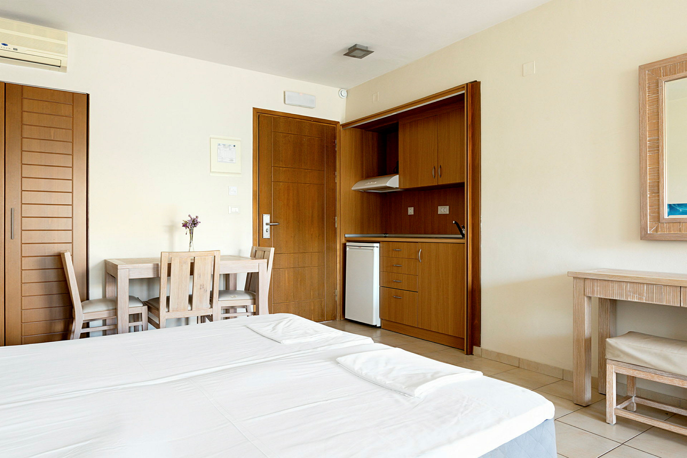 Hotellihuone, jossa on parisänky, pieni keittiö puusisustuksella, ruokapöytä kahdella tuolilla ja peili kirjoituspöydän yläpuolella. (Tekoälyn luoma teksti)