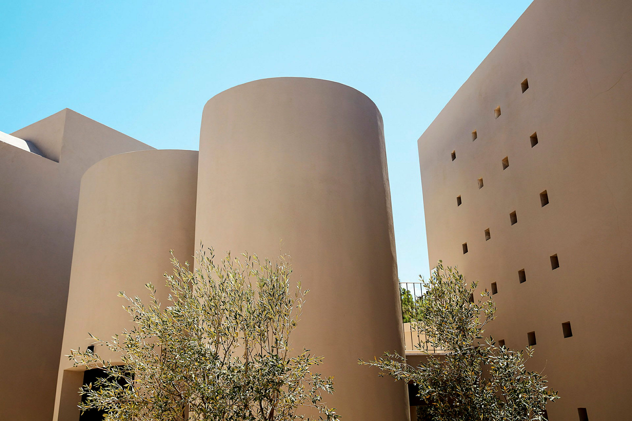 Kuvassa on moderni rakennus, jossa on lieriömäisiä rakenteita ja beigejä julkisivuja sekä puita etualalla. (Tekoälyn luoma teksti)