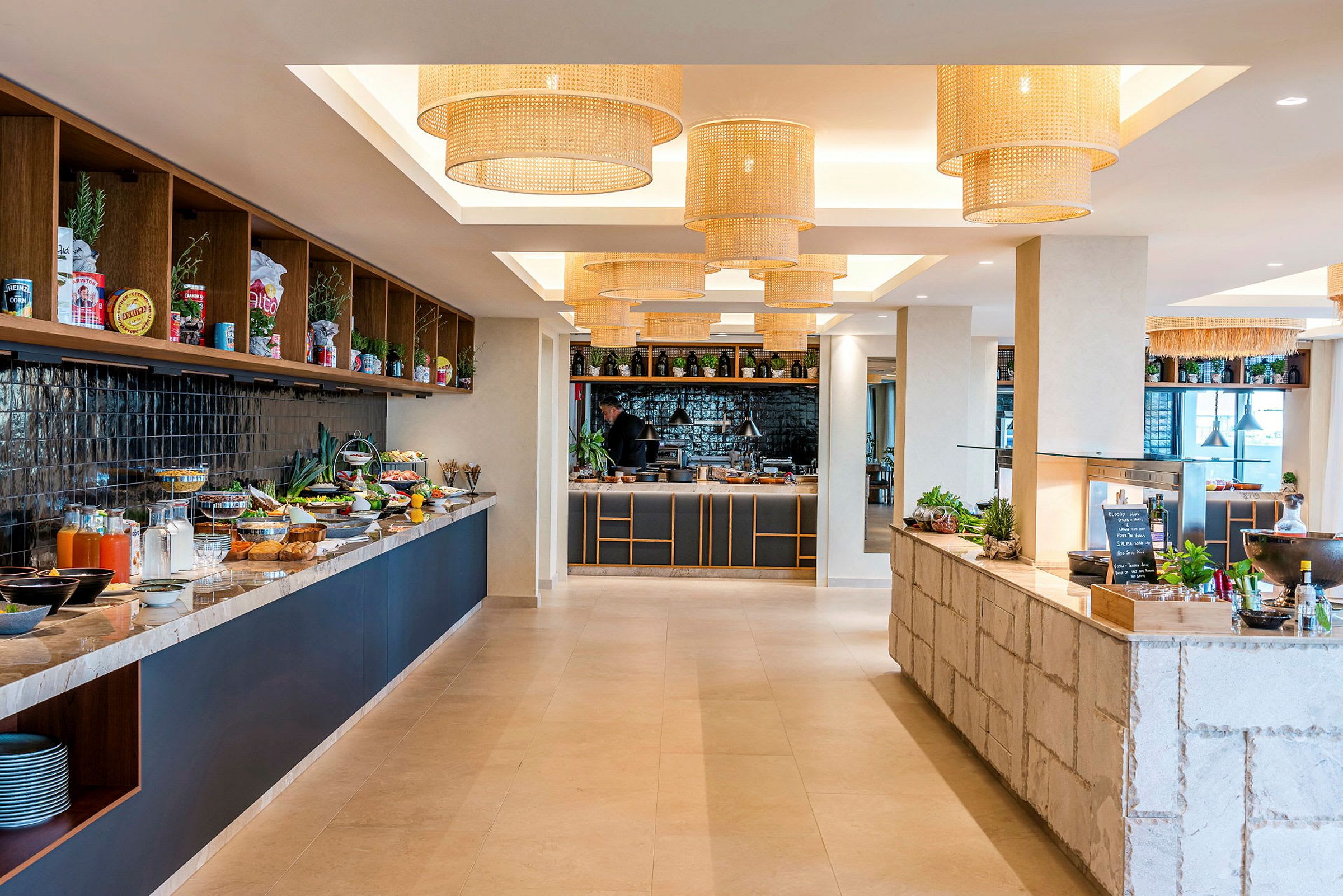 Kuva modernista buffet-ruokasalista, jossa ruokia ja juomia on aseteltu pöydille, sekä koristeellisia kattovalaisimia. (Tekoälyn luoma teksti)