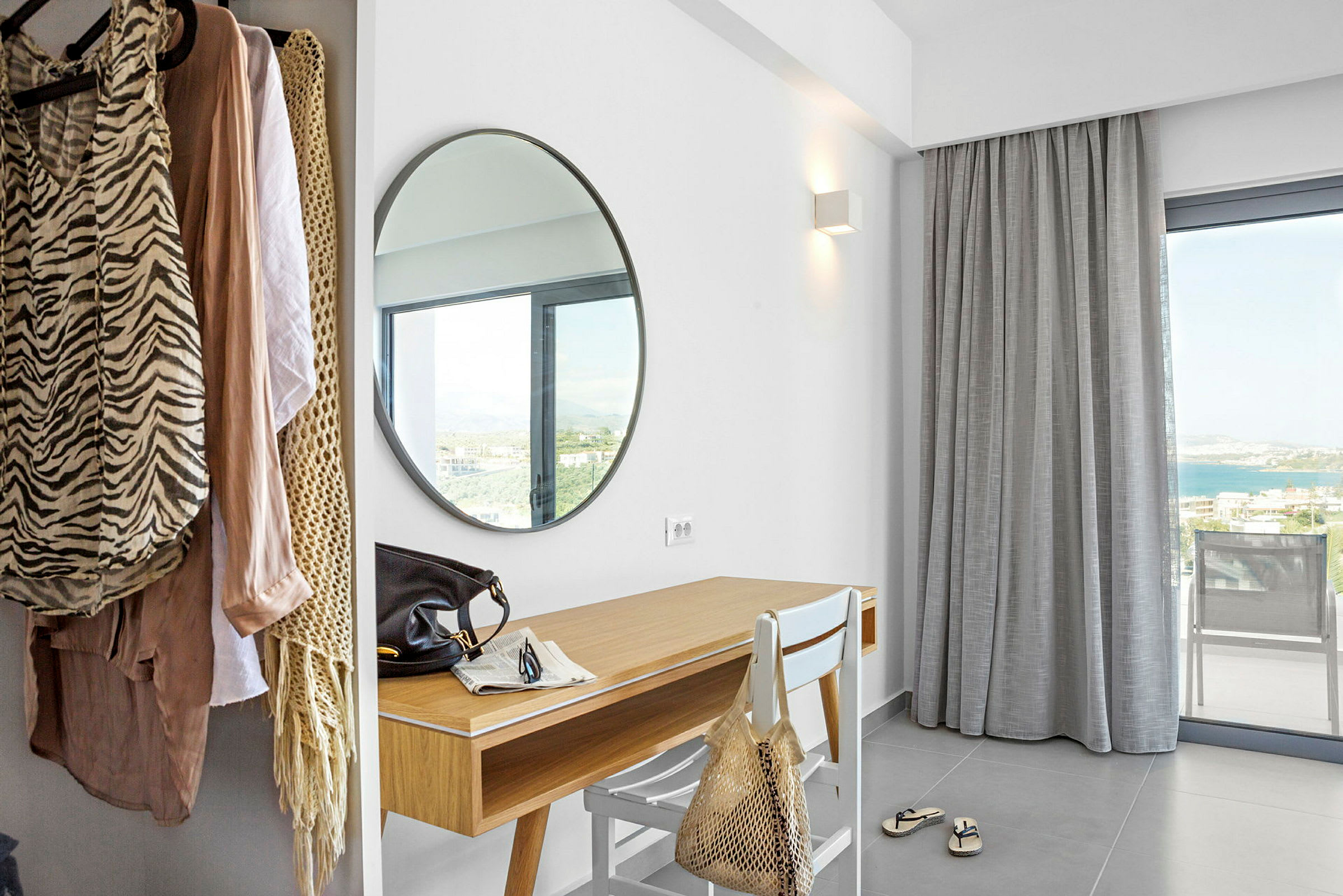 Hotellihuone, jossa on pyöreä peili, kirjoituspöytä ja vaateripustin. (Tekoälyn luoma teksti)