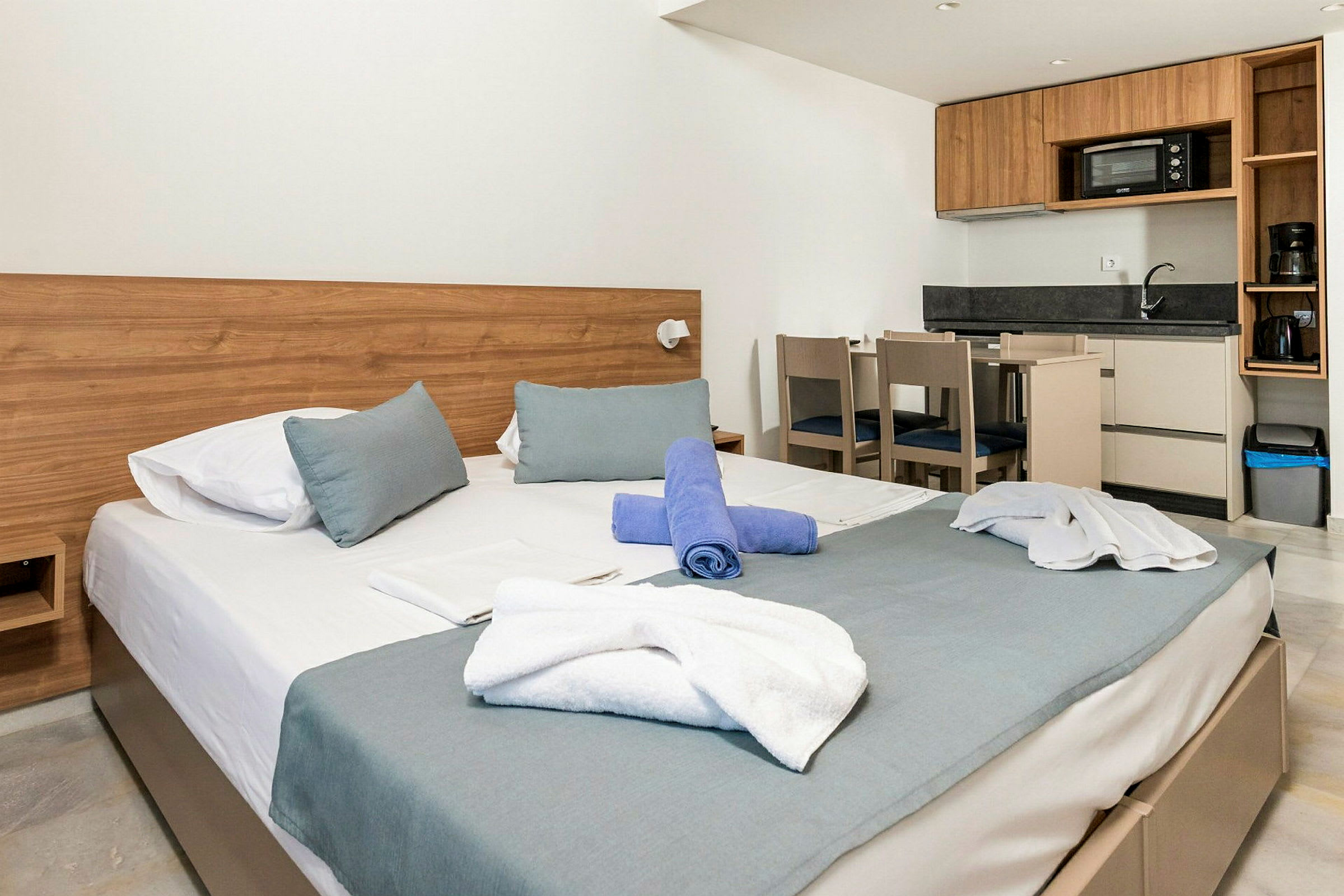 Modernisti sisustettu hotellihuone, jossa sänky, keittiö ja ruokapöytä. (Tekoälyn luoma teksti)