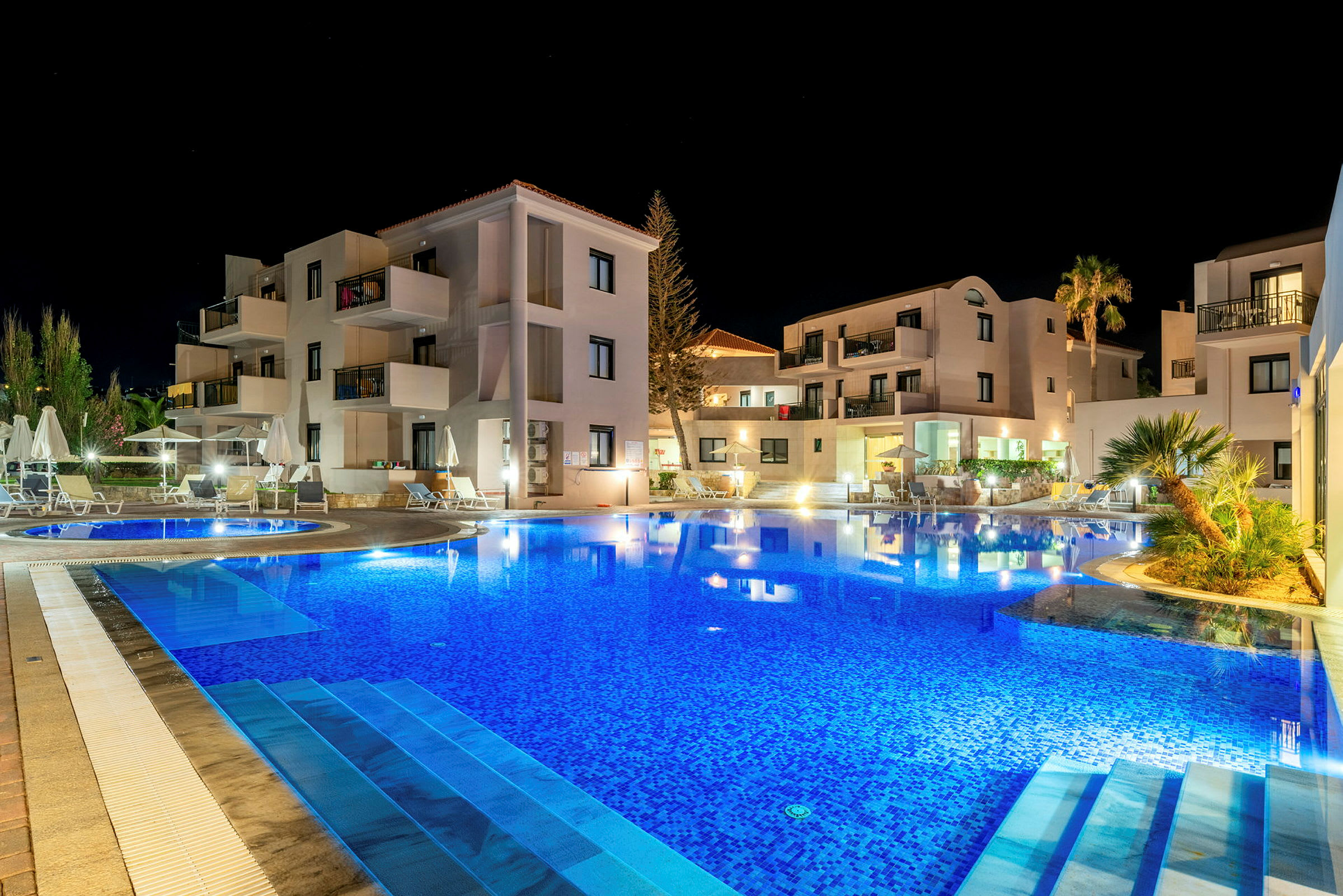 Hotellirakennus valaistuna illalla, etualalla uima-allas. (Tekoälyn luoma teksti)