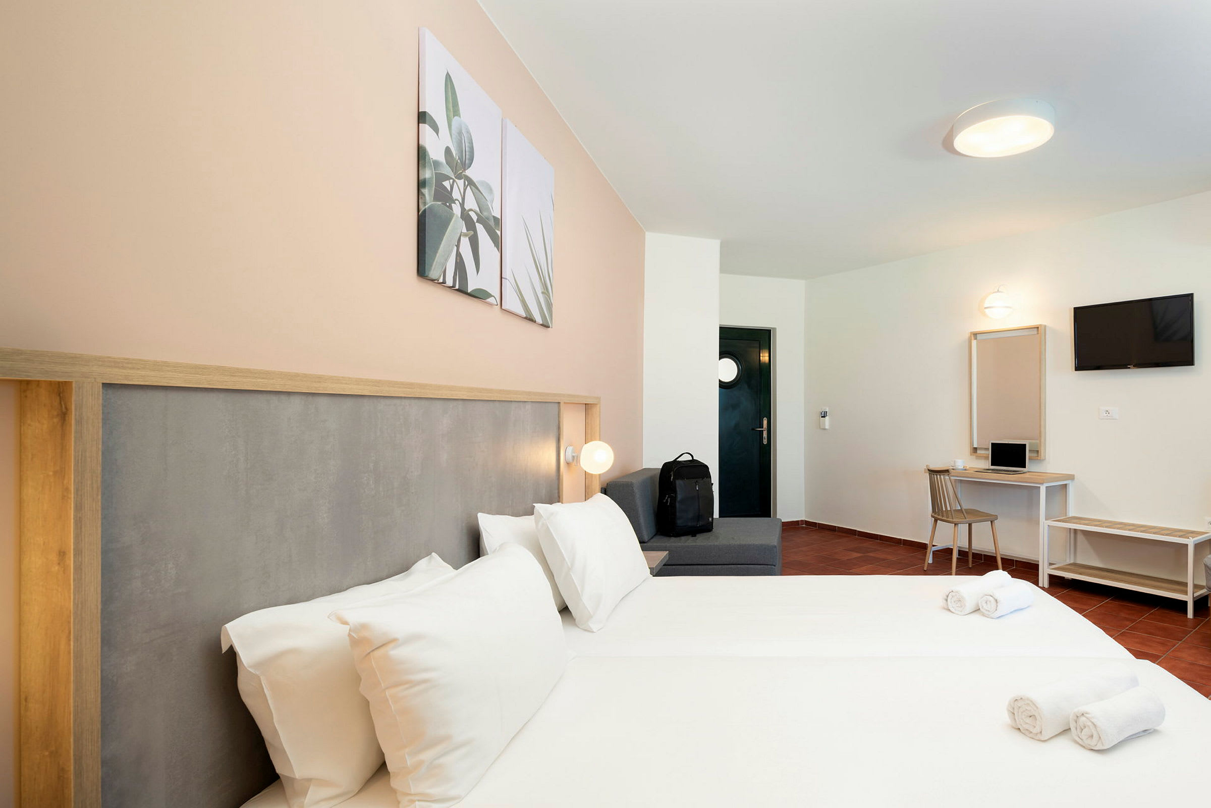 Hotellihuone, jossa parivuode, istuinalue, työpöytä ja TV. (Tekoälyn luoma teksti)