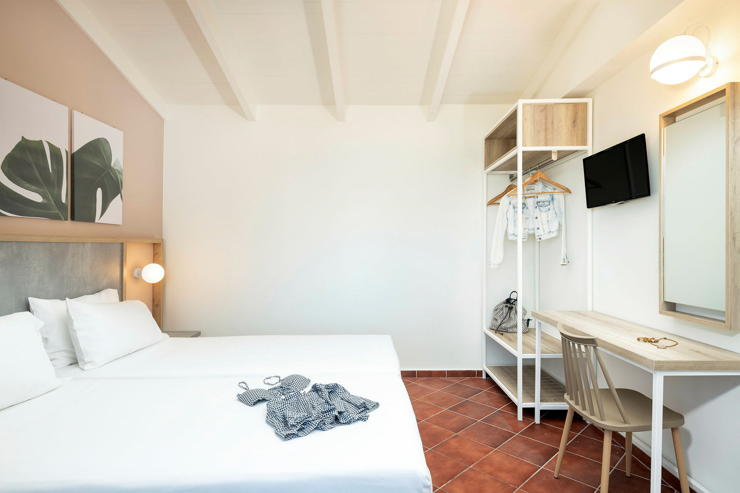 Hotellihuone, jossa parisänky, kirjoituspöytä, tuoli ja avoin vaateteline. (Tekoälyn luoma teksti)