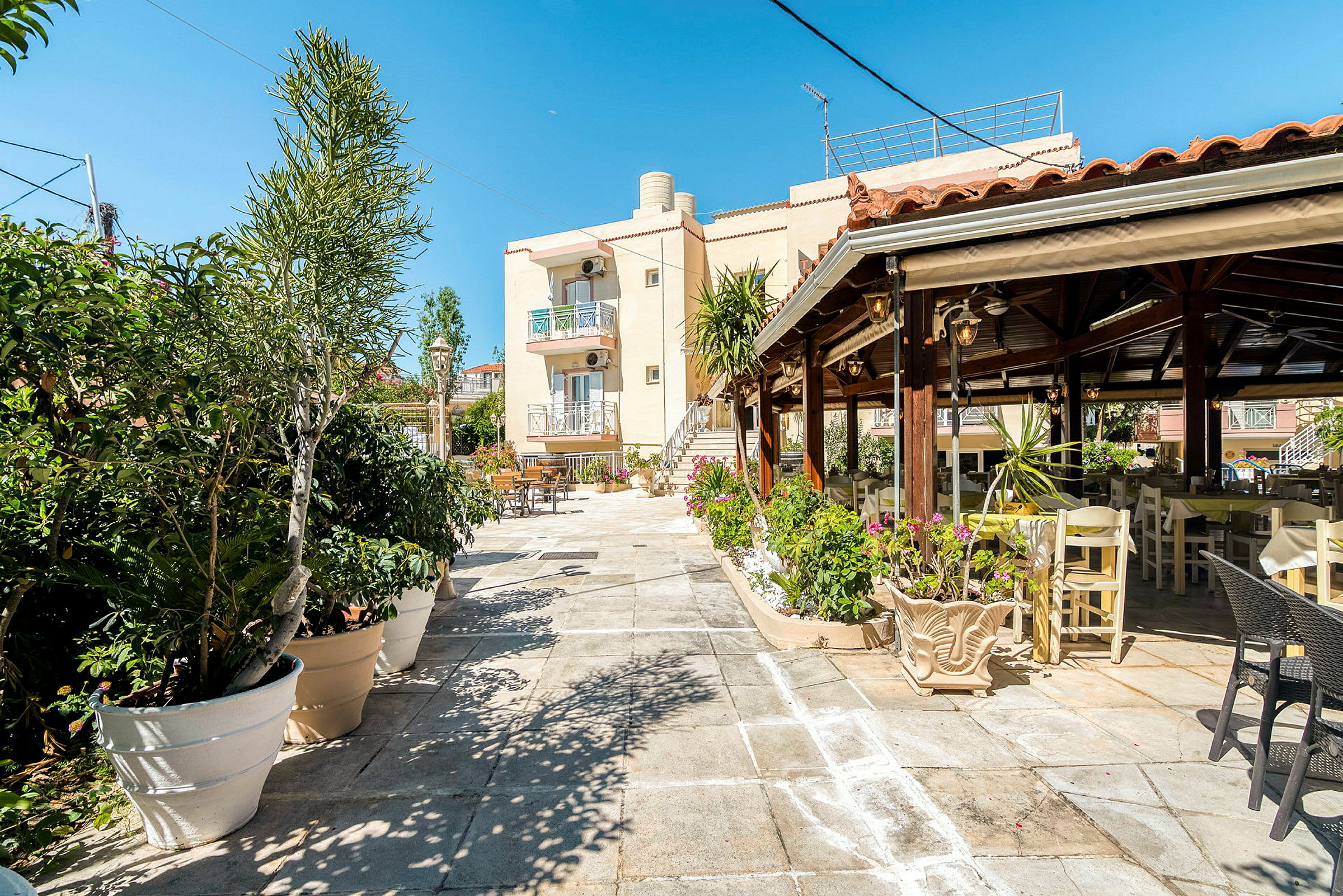 Piha-alue, jossa on pöytiä ja tuoleja, ympärillä ruukkukasveja, ja taustalla rakennus. (Tekoälyn luoma teksti)