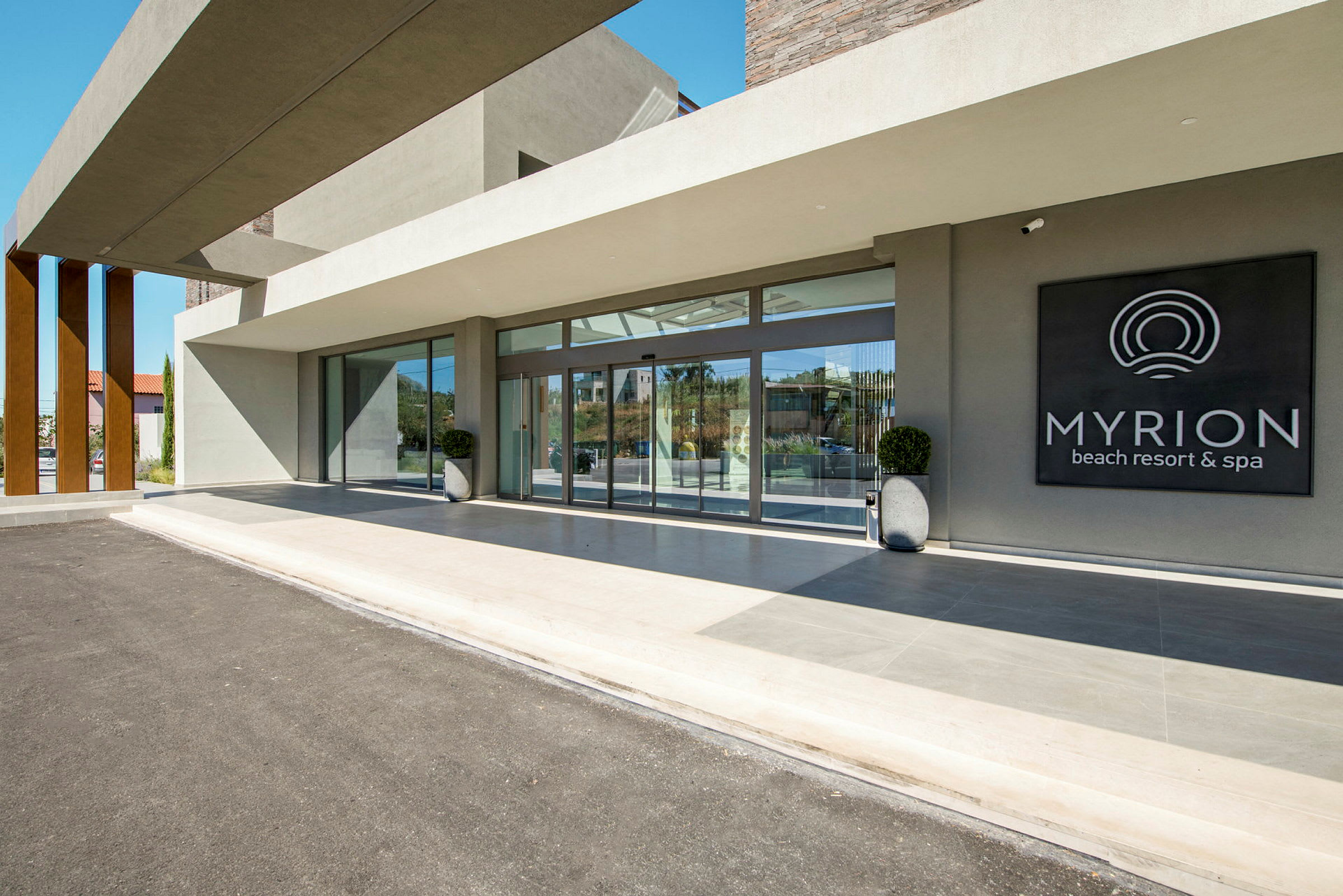 Myrion Beach Resort & Spa -sisäänkäynti lasiseinillä ja kyltillä. (Tekoälyn luoma teksti)