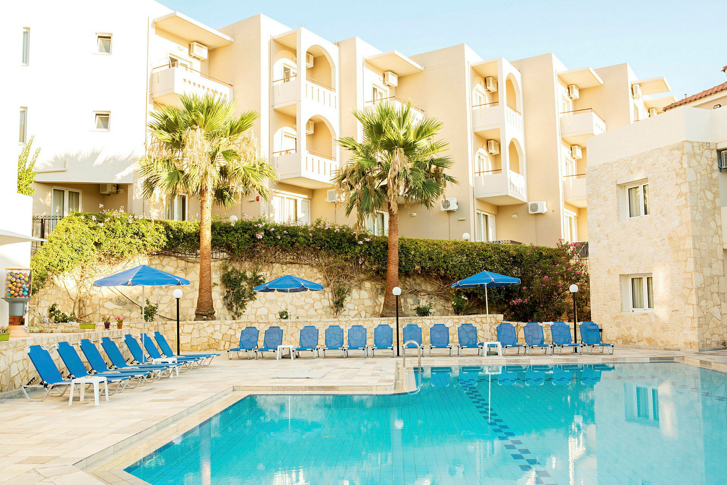 Hotellirakennus, jossa on parvekkeita uima-altaan vieressä, aurinkotuoleja ja varjoja. (Tekoälyn luoma teksti)