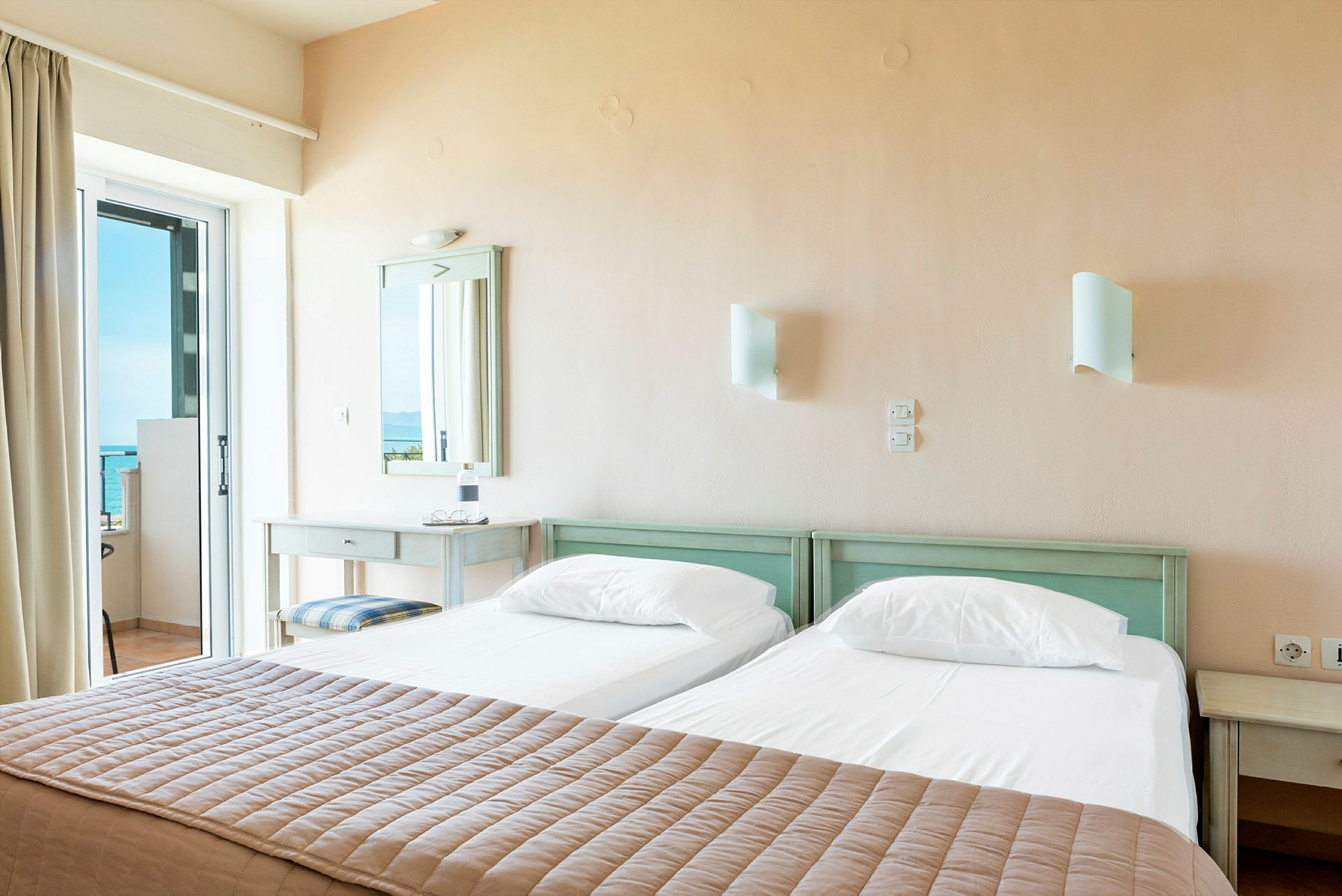 Hotellihuone, jossa on kaksi erillistä vuodetta ja näkymä merelle lasioven kautta. (Tekoälyn luoma teksti)