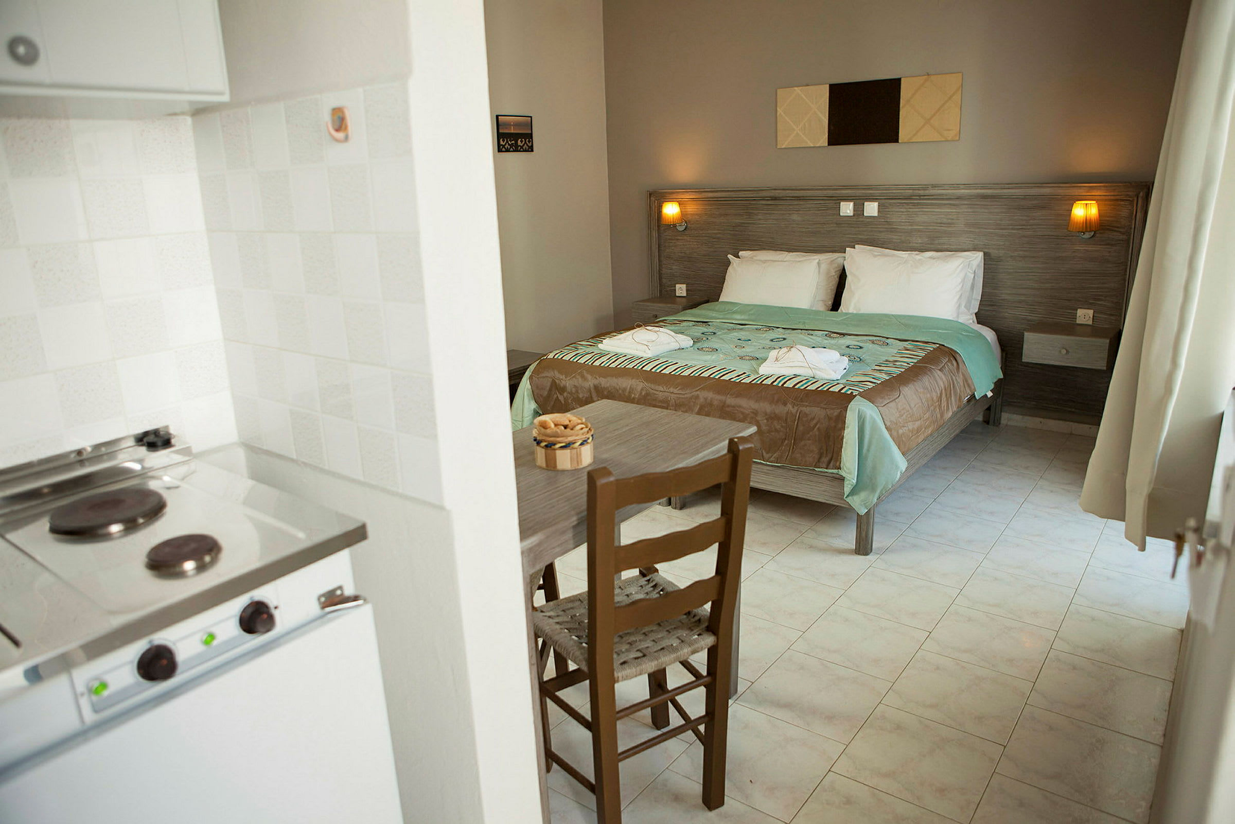 Hotellihuone, jossa on parivuode, pöytä, tuoli ja pieni keittiötila. (Tekoälyn luoma teksti)