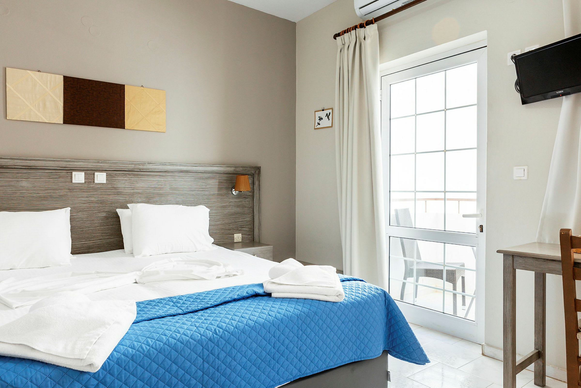 Hotellihuone, jossa parisänky, sininen päiväpeite ja valkoiset vuodevaatteet. (Tekoälyn luoma teksti)