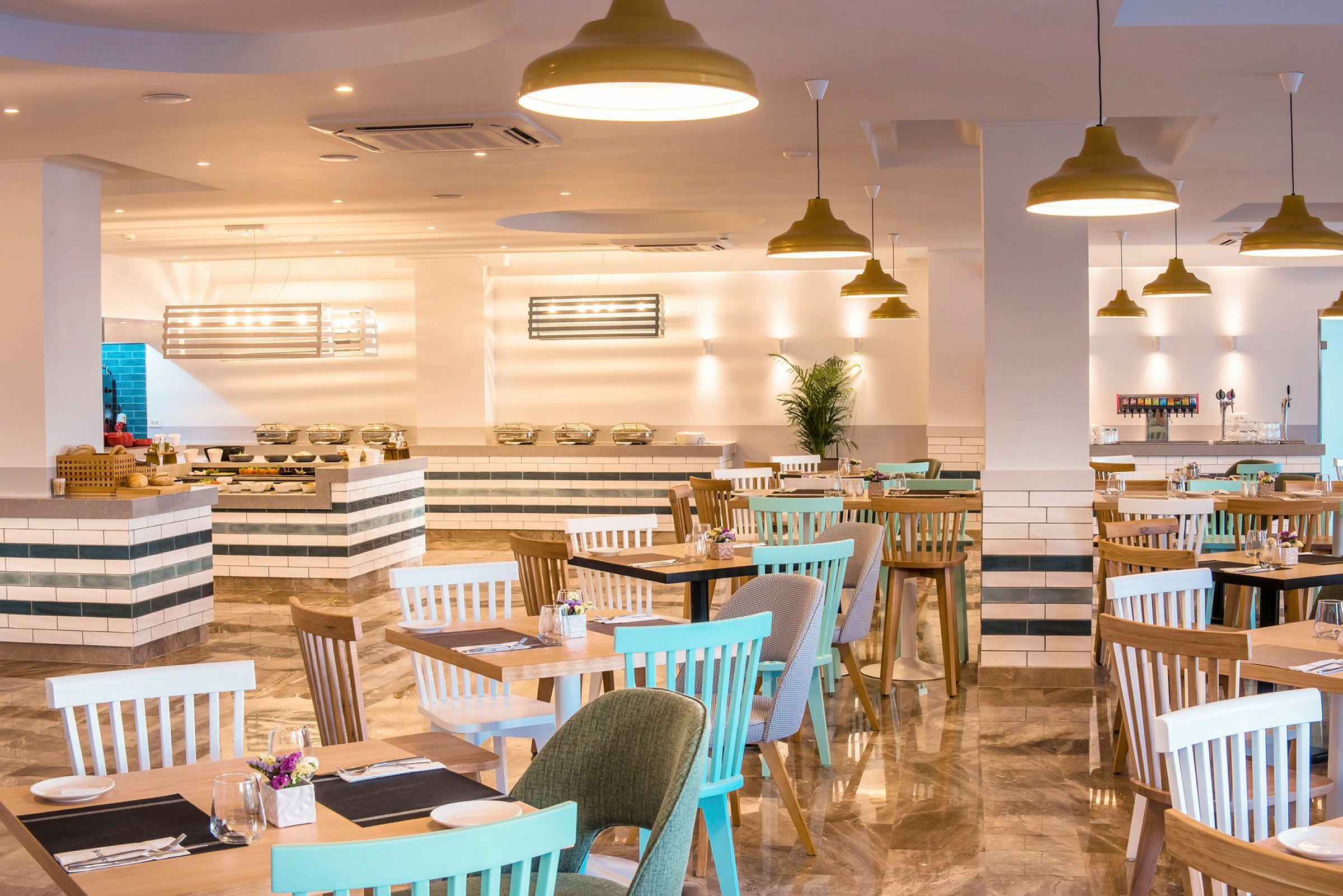 Vaalea ruokailutila, jossa pöytiä ja tuoleja, sekä buffet tarjoilualue taustalla. (Tekoälyn luoma teksti)