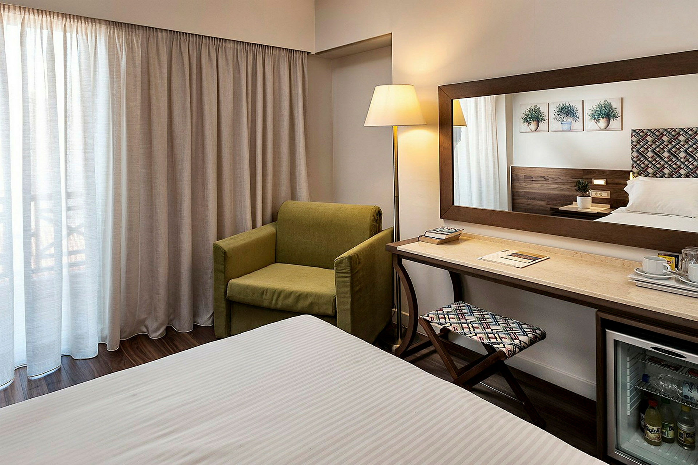 Hotellihuone vihreällä nojatuolilla, kirjoituspöydällä, peilillä ja sängyllä. (Tekoälyn luoma teksti)