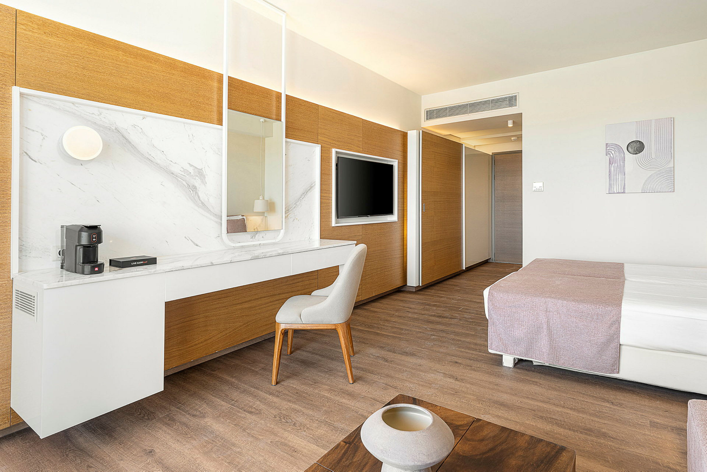 Moderni hotellihuone, jossa on työpöytä ja peili, sänky ja televisio. (Tekoälyn luoma teksti)