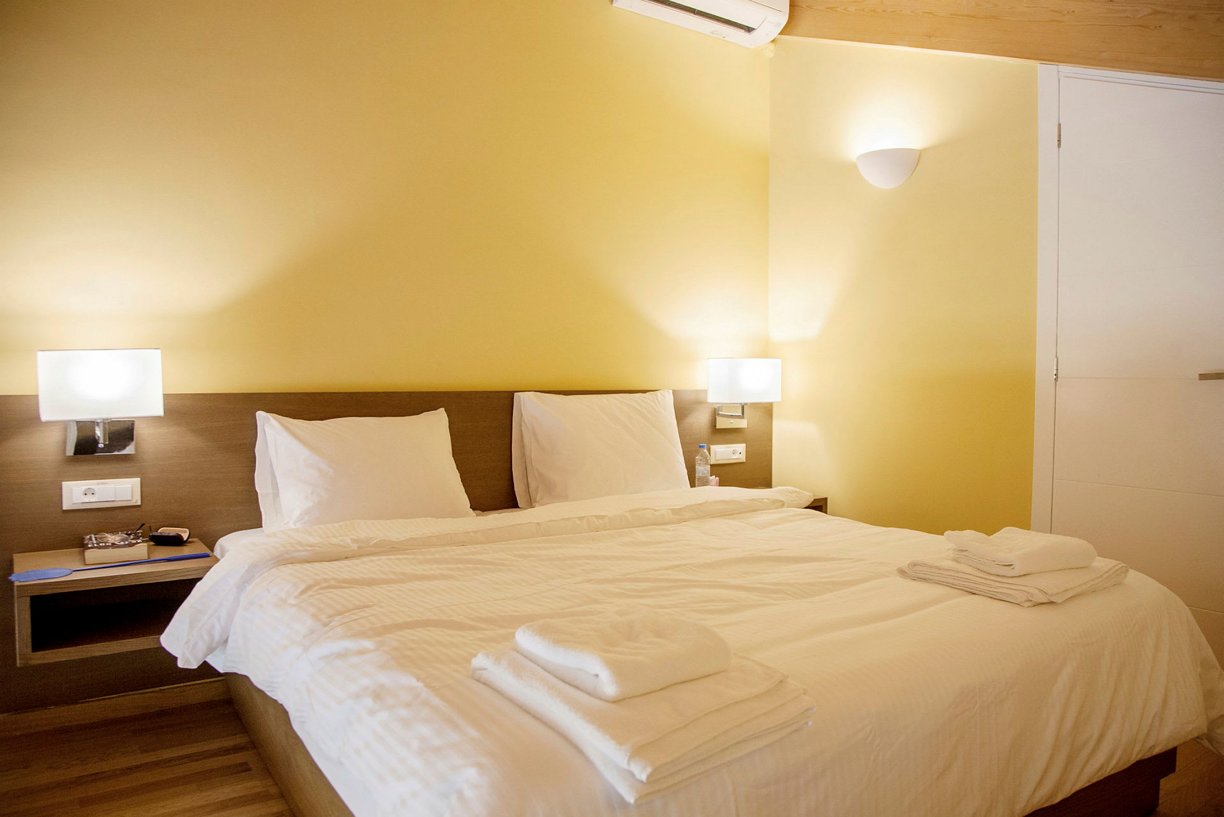Hotellihuone, jossa on parivuode, valkoiset vuodevaatteet ja keltaiset seinät. (Tekoälyn luoma teksti)