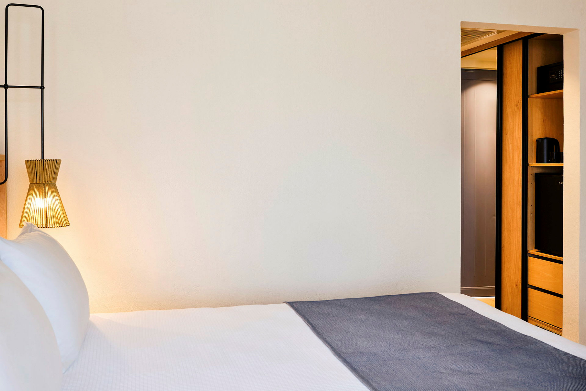 Hotellihuone, jossa on sänky, nykyaikainen lamppu ja osa sisustuksesta säilytystilalla. (Tekoälyn luoma teksti)