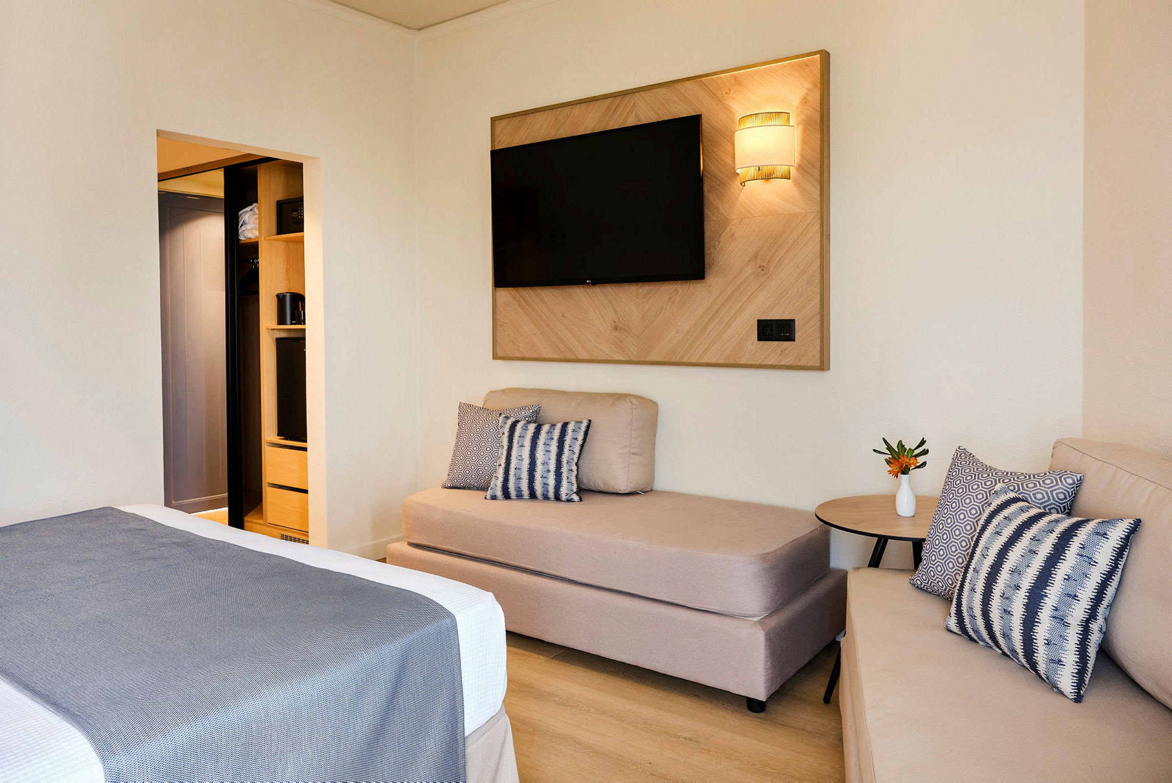 Hotellihuone, jossa sohva, sänky ja TV seinällä. (Tekoälyn luoma teksti)