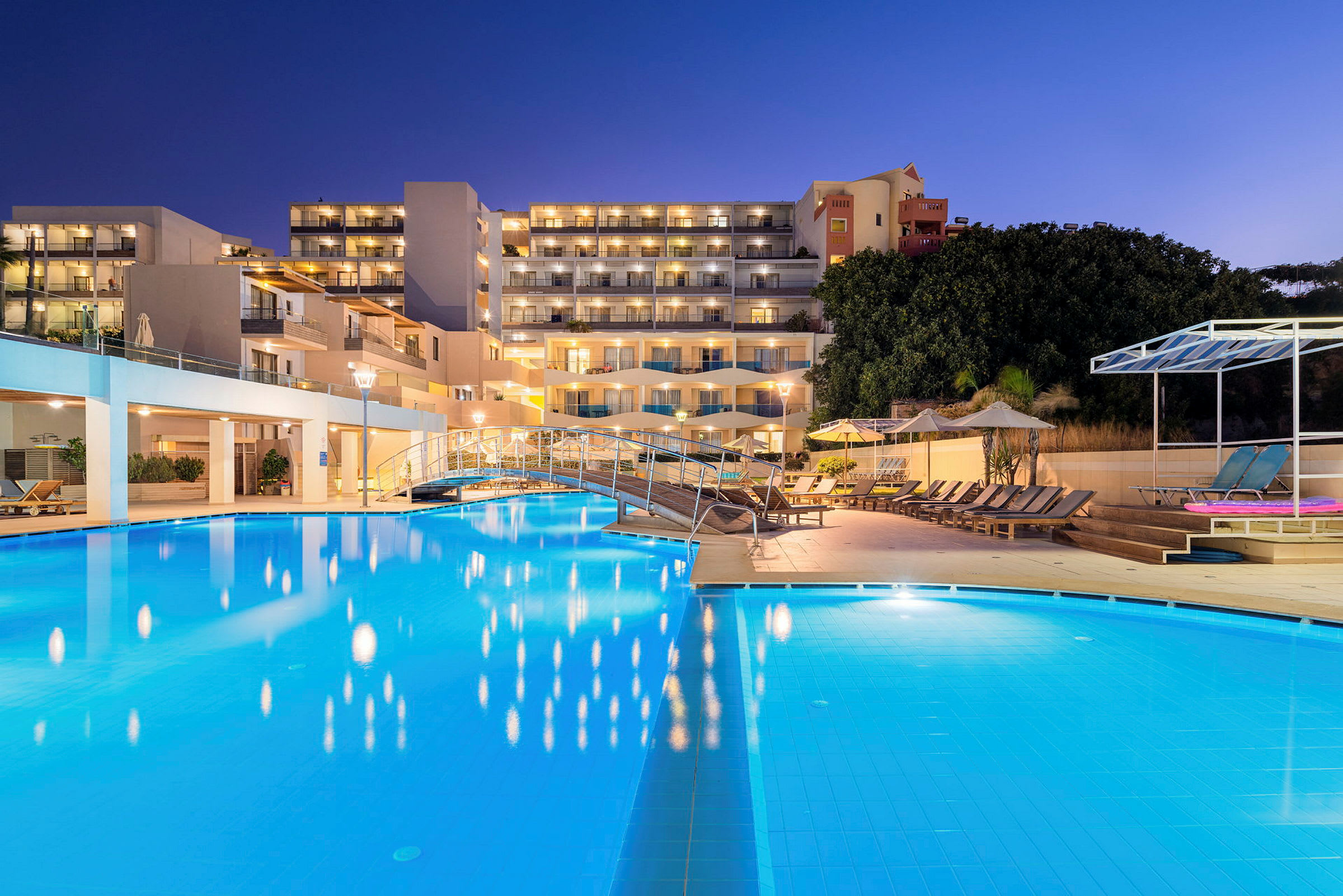 Hotellialue, jossa valaistu uima-allas ja aurinkotuoleja illalla. (Tekoälyn luoma teksti)