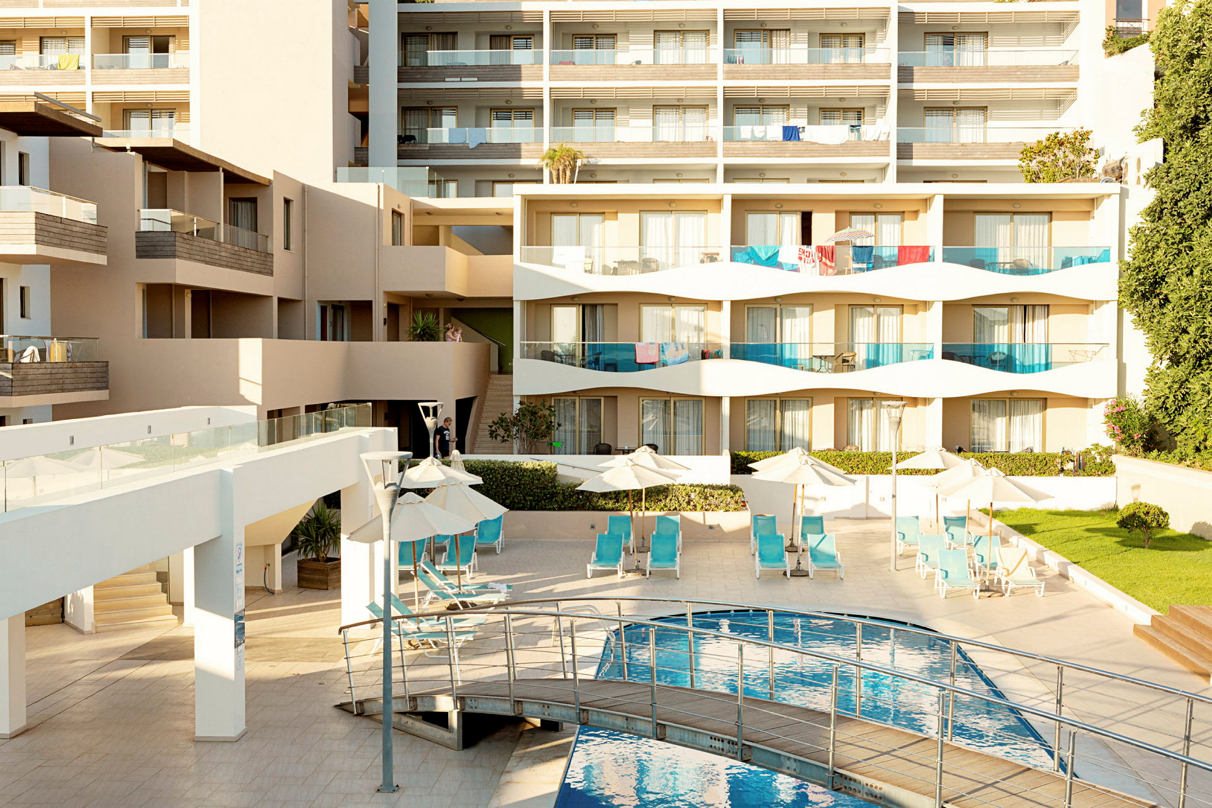 Moderni hotellirakennus, jossa on parvekkeita, aurinkotuoleja altaan äärellä ja viheralueita. (Tekoälyn luoma teksti)