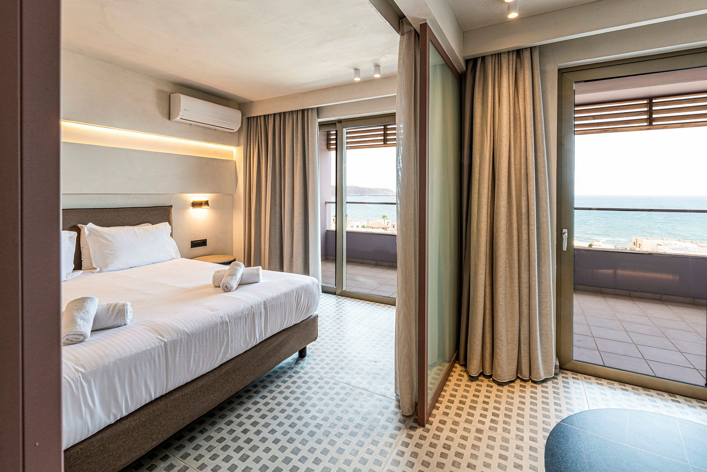 Hotellihuone, jossa sänky ja pyyhkeet. Suuret lasiovet johtavat parvekkeelle, jolta näkyy meri. (Tekoälyn luoma teksti)