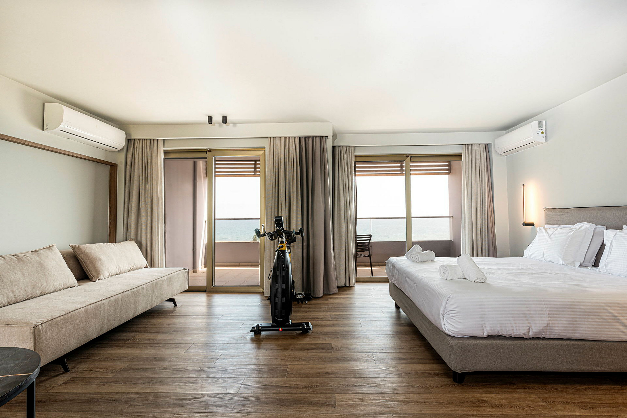 Hotellihuone, jossa on sänky ja sohva, näkymä parvekkeelle ja merelle. (Tekoälyn luoma teksti)
