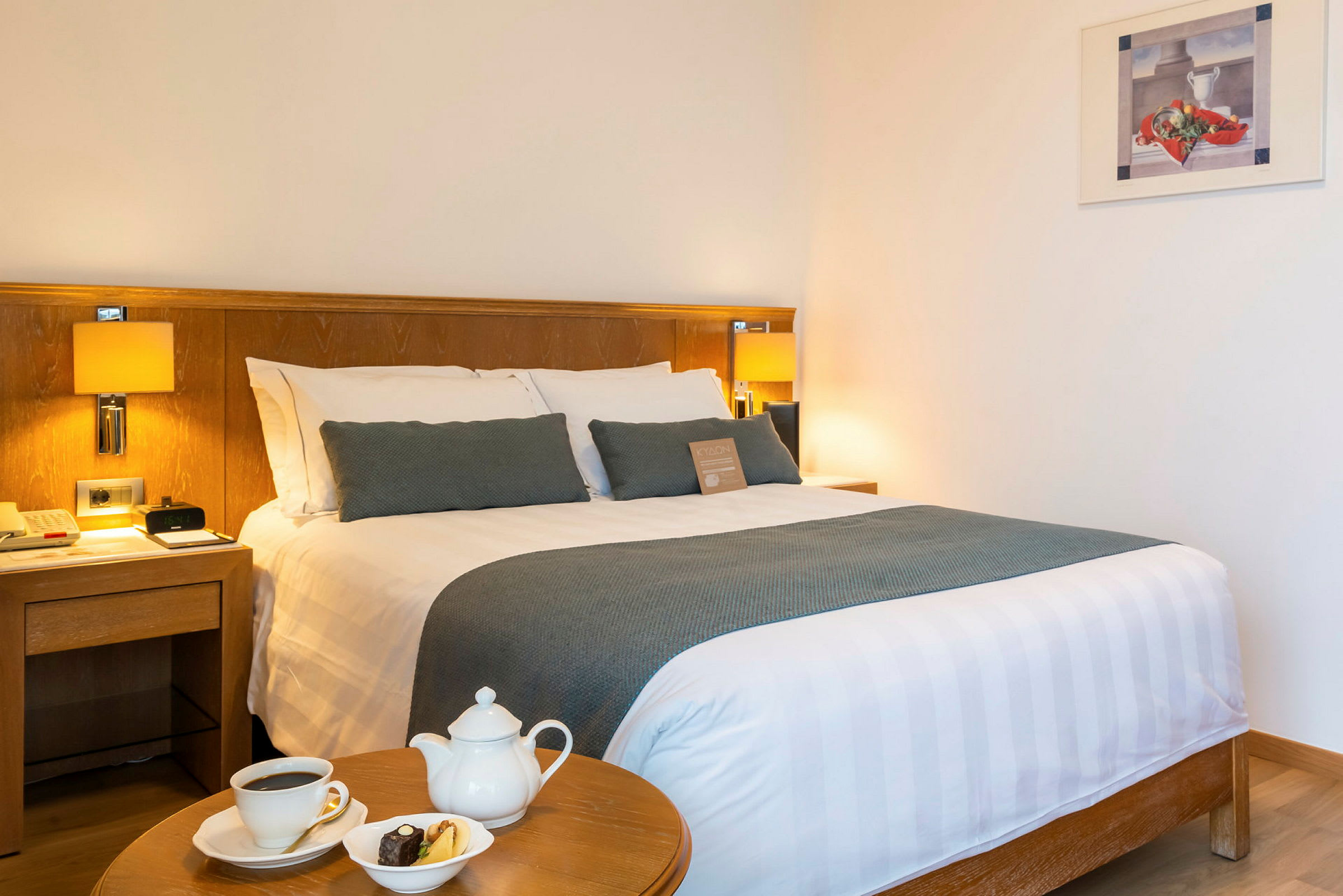 Hotellihuone, jossa on parisänky, yöpöytä ja pöytä, jossa kahvikuppi, teekannu ja lautanen keksejä. (Tekoälyn luoma teksti)