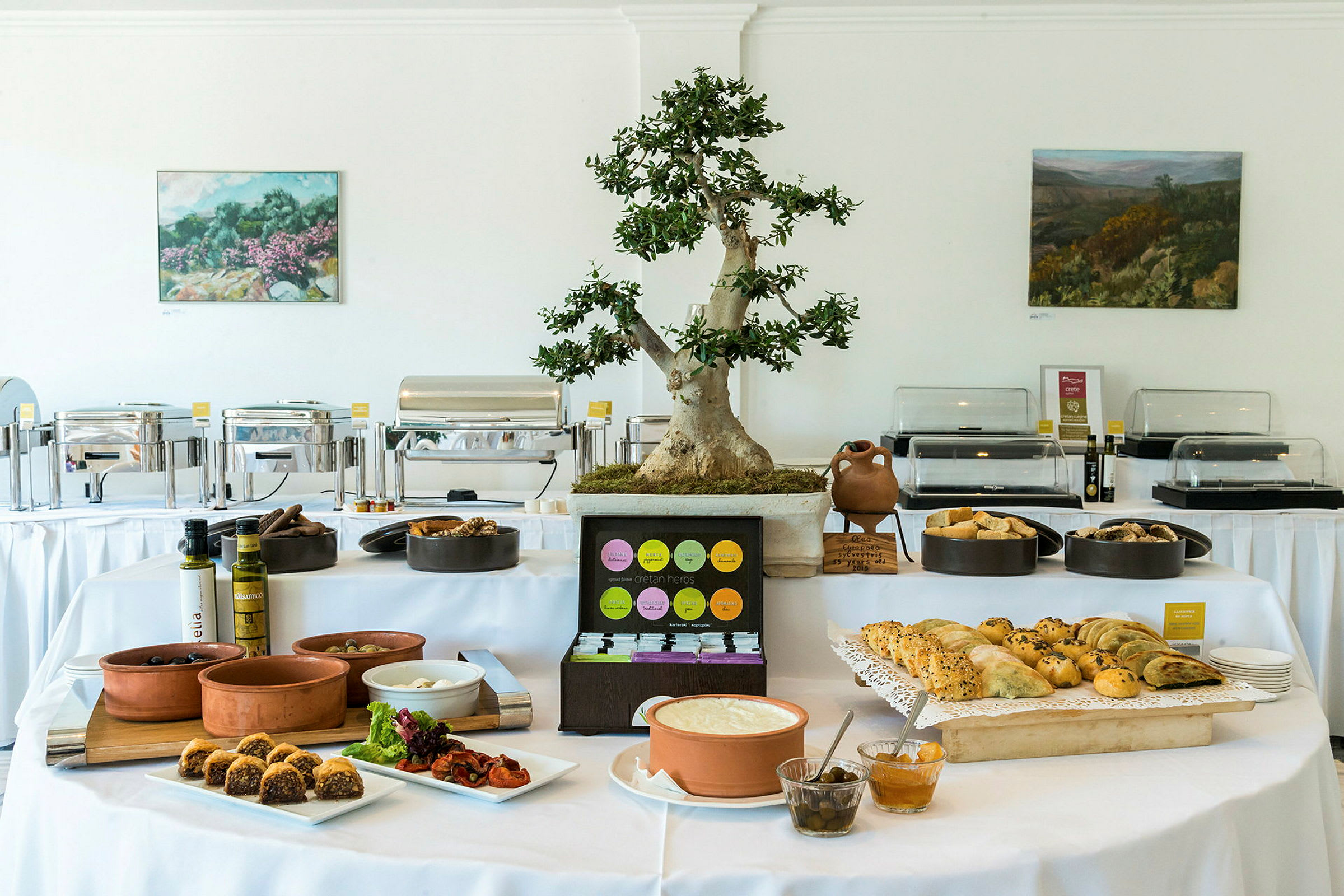 Buffet-huone, jossa on katettu pöytä erilaisilla ruoilla ja koristeellinen ruukkukasvi pöydällä. (Tekoälyn luoma teksti)