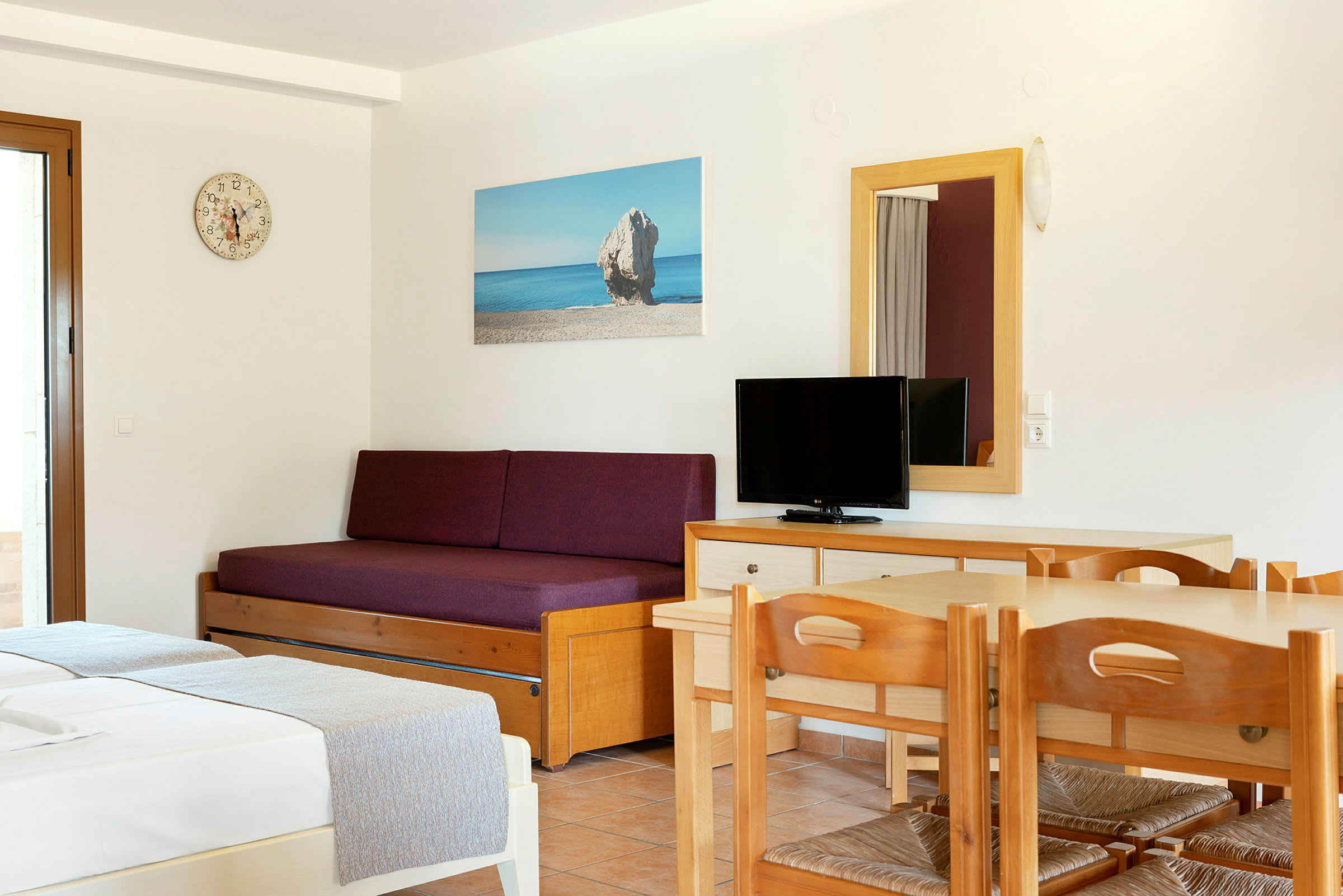 Hotellihuoneen sisustus, jossa on vuodesohva, pöytä tuoleineen ja televisio. (Tekoälyn luoma teksti)