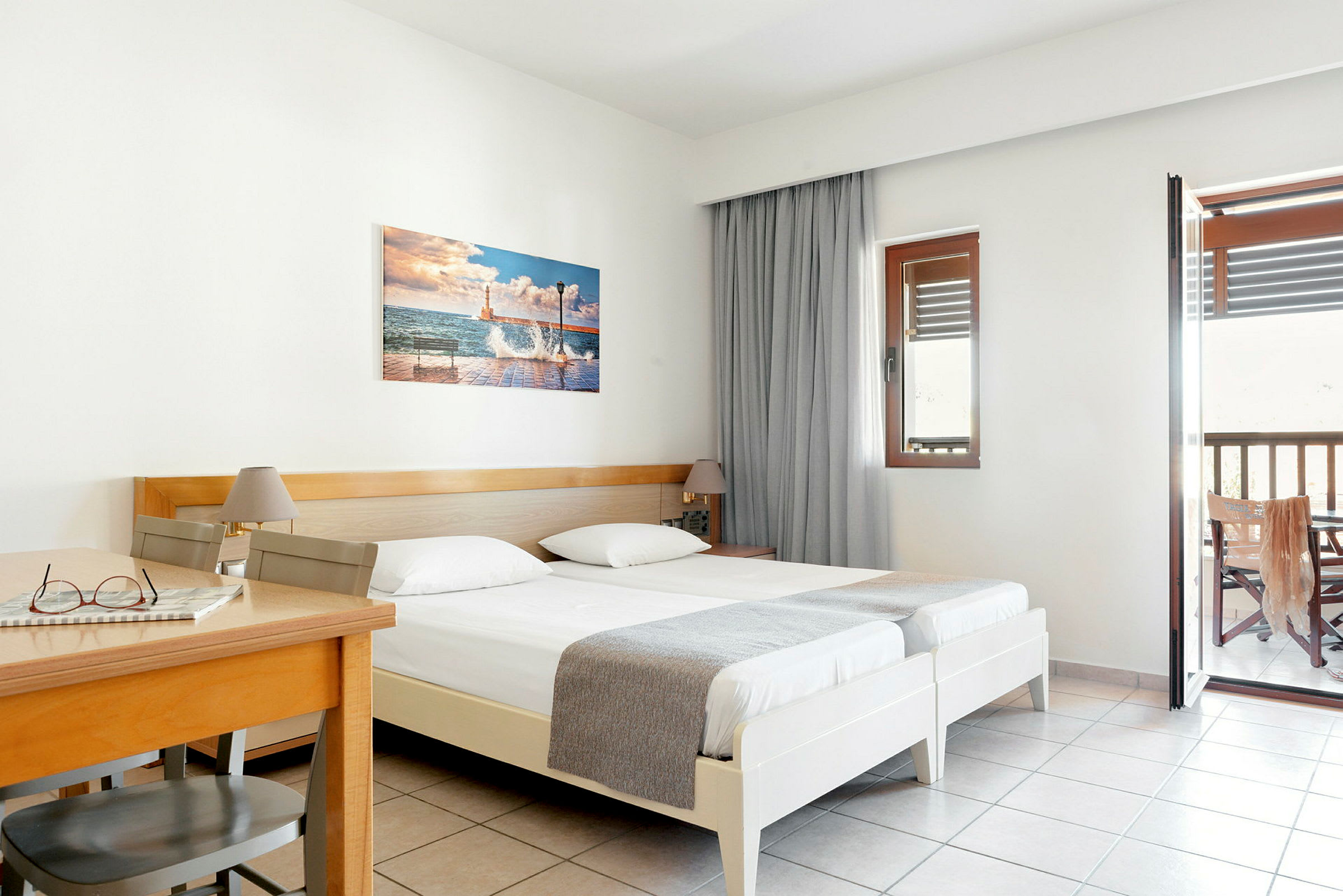 Hotellihuone, jossa kaksi erillistä vuodetta, puupöytä ja tuoli sekä parveke. (Tekoälyn luoma teksti)