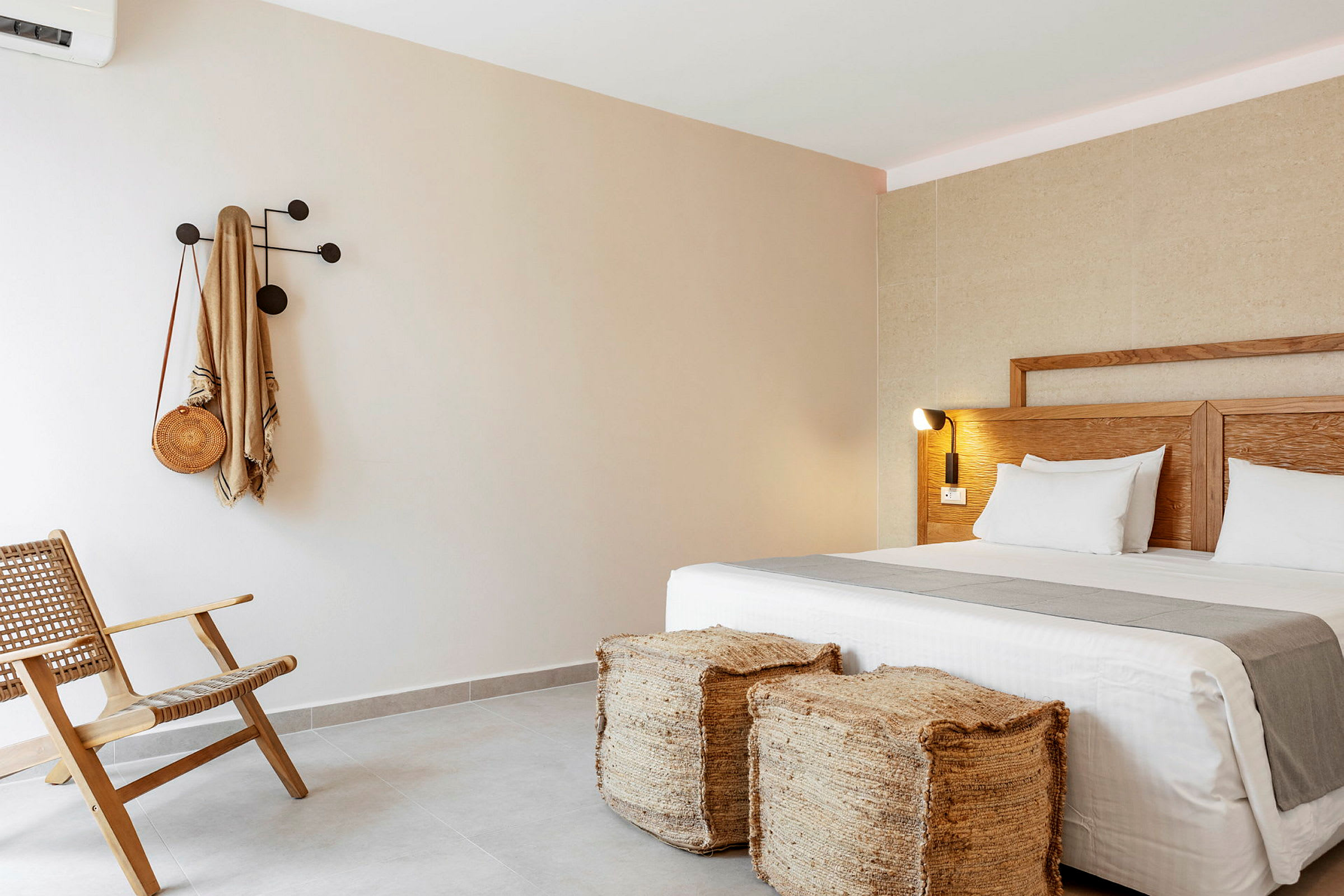 Hotellihuone, jossa on moderni sisustus, sisältäen sängyn, kaksi jakkaraa, tuolin ja seinäkoukun. (Tekoälyn luoma teksti)