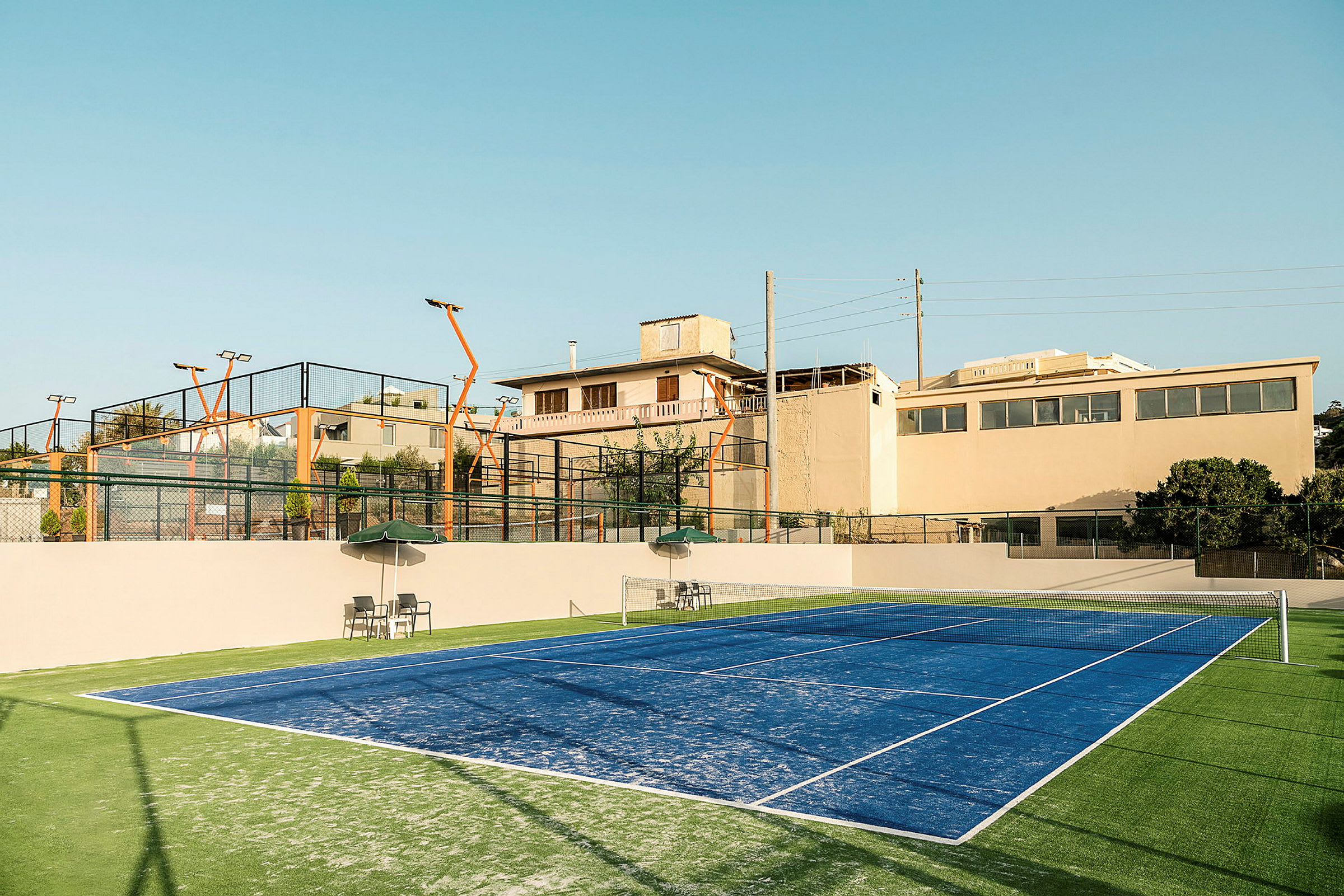 Sininen padelkenttä, taustalla katsomot ja ympäröivät rakennukset. (Tekoälyn luoma teksti)
