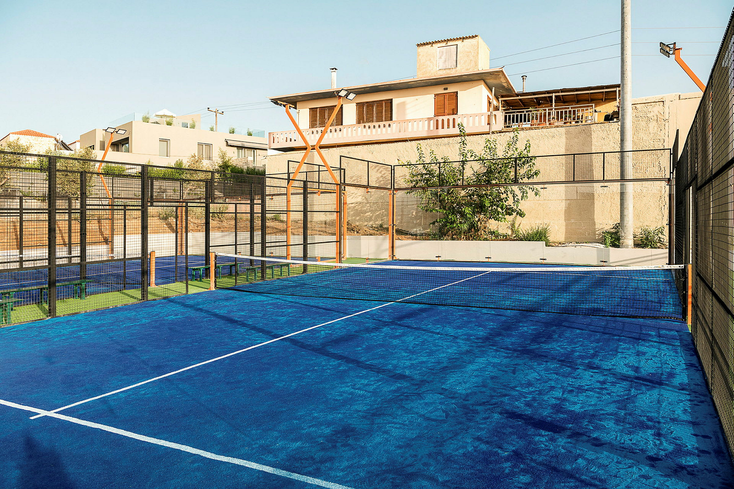 Sininen padel-kenttä, jossa on verkko ja ympäröiviä rakennuksia. (Tekoälyn luoma teksti)