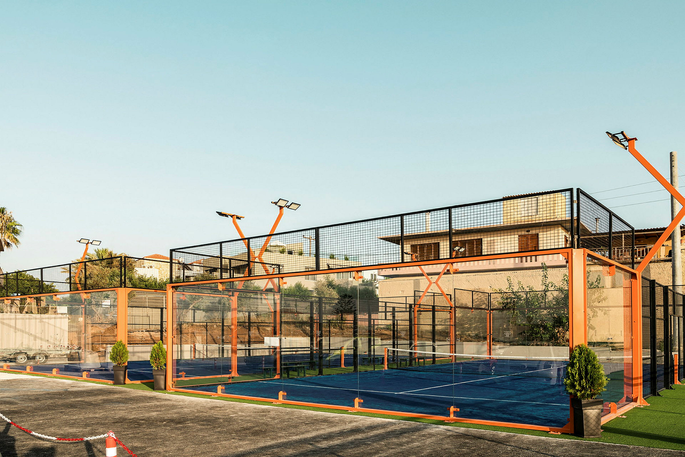 Lasilla ja oranssilla kehikolla ympäröity ulkona sijaitseva padelkenttä. (Tekoälyn luoma teksti)