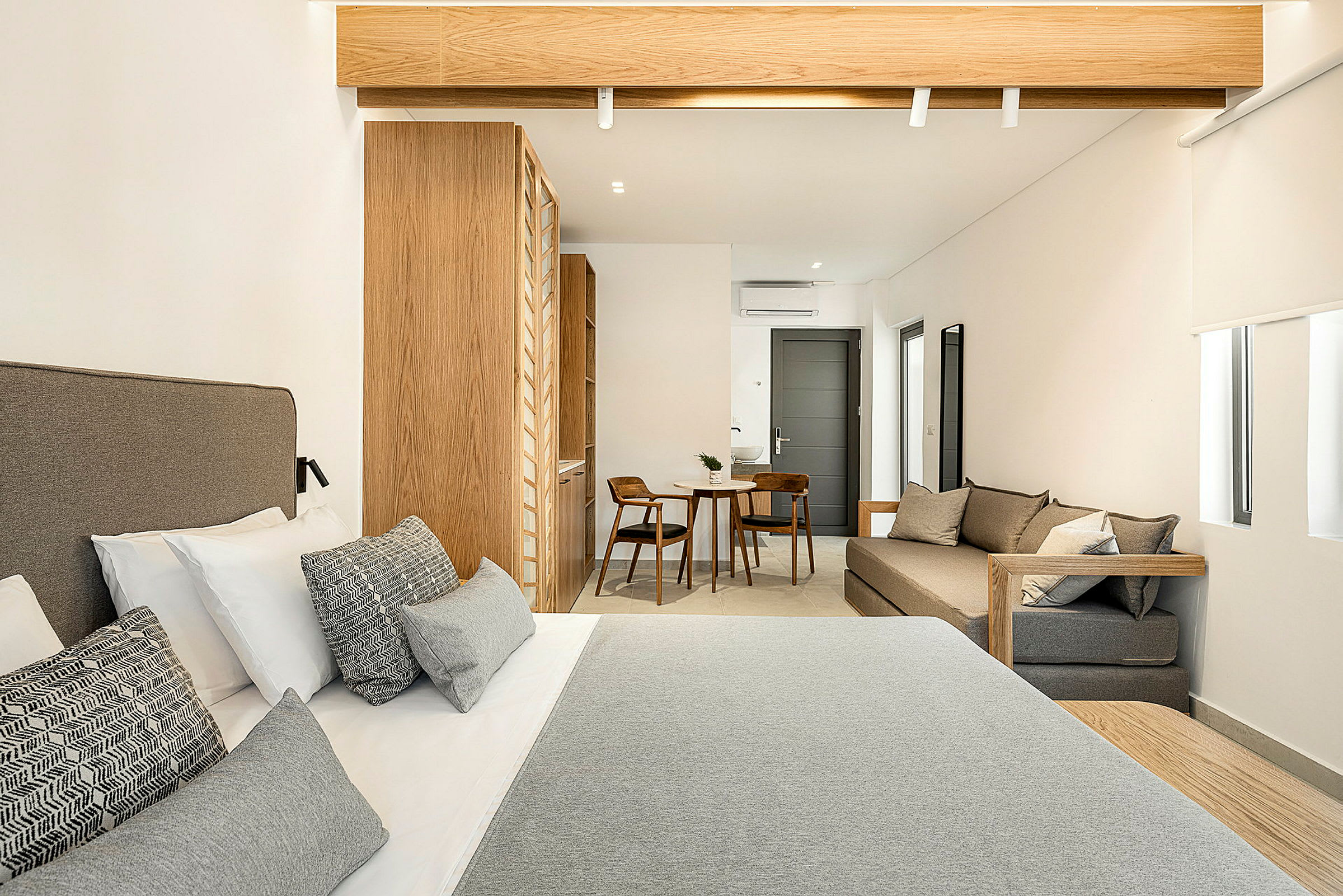 Hotellihuone, jossa on parisänky etualalla, puusisustus ja pieni istuma-alue, jossa pöytä ja kaksi tuolia taustalla. (Tekoälyn luoma teksti)