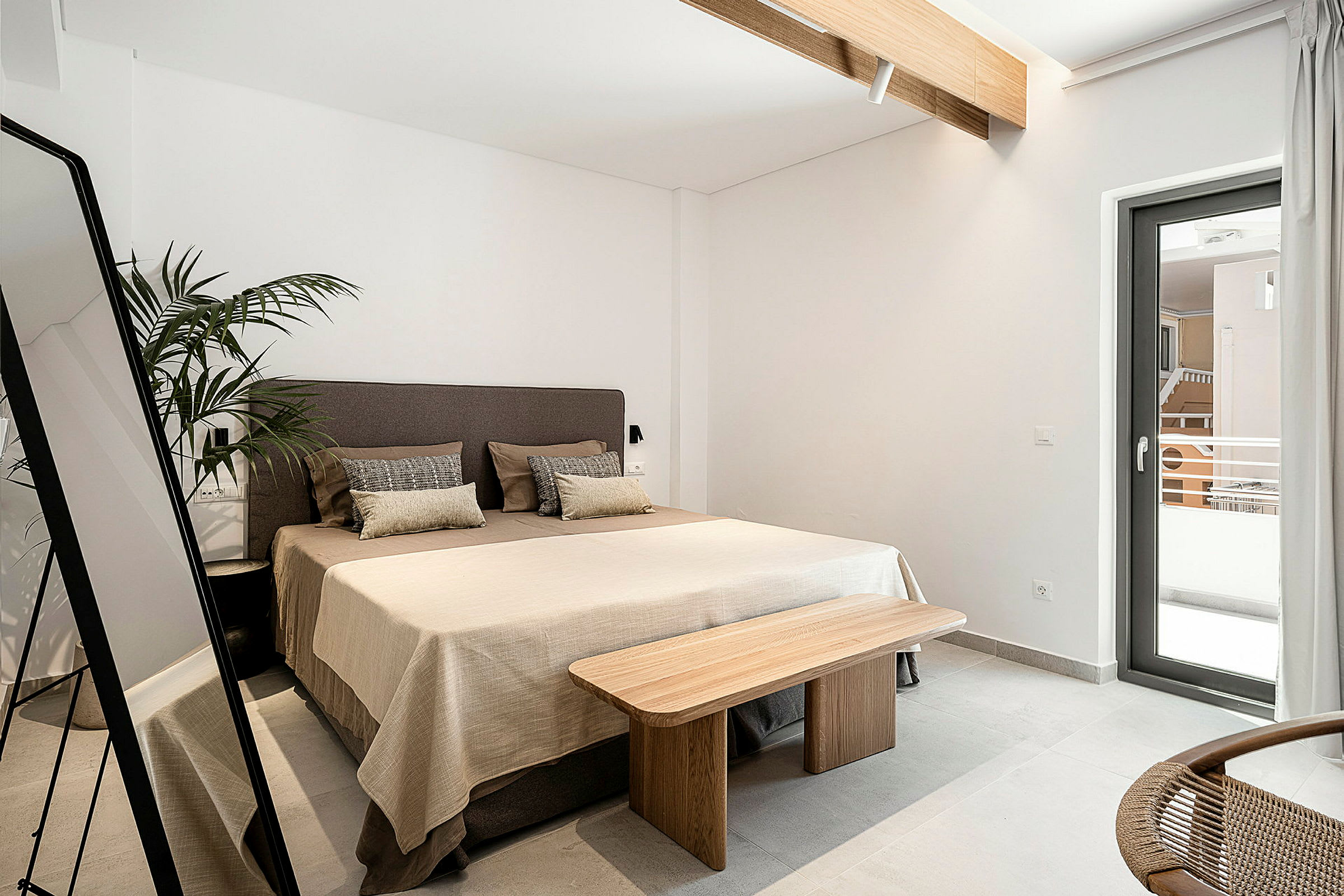 Hotellihuone, jossa on sänky, peili, kasvi ja ikkuna, joka avautuu parvekkeelle. (Tekoälyn luoma teksti)