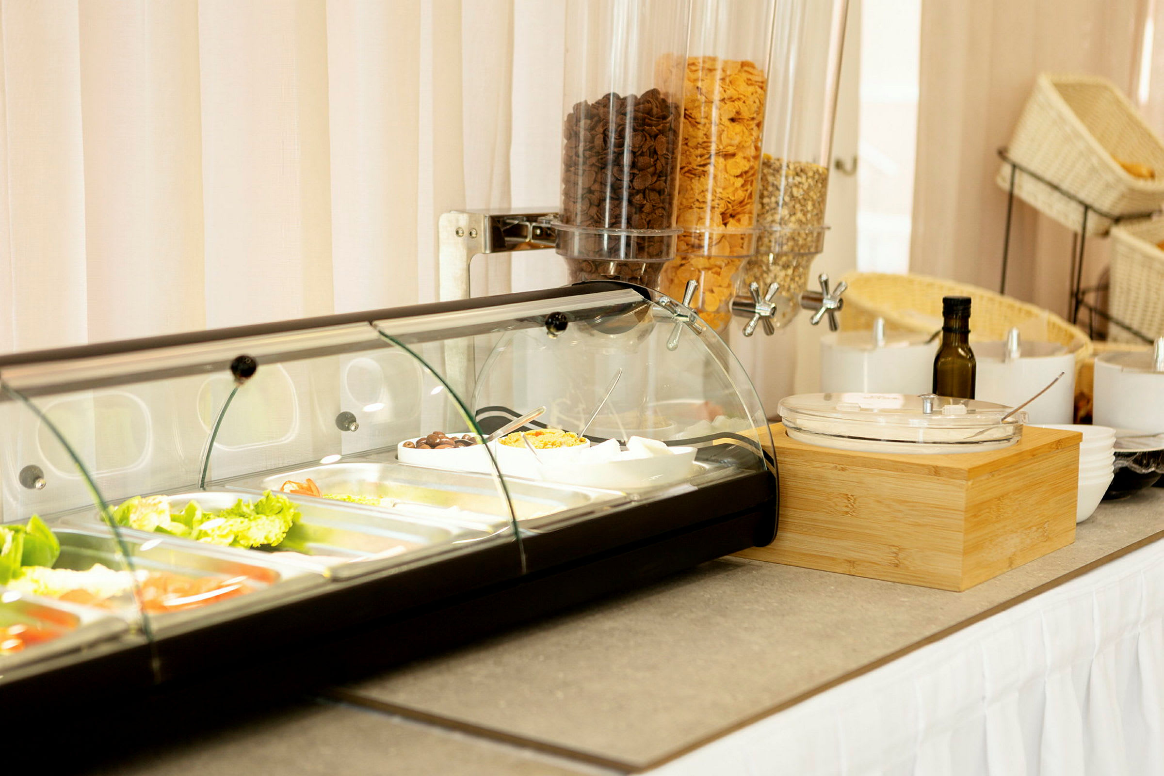 Buffet, jossa on salaattitarvikkeita lasiastioissa ja viljaa annostelijoissa. (Tekoälyn luoma teksti)