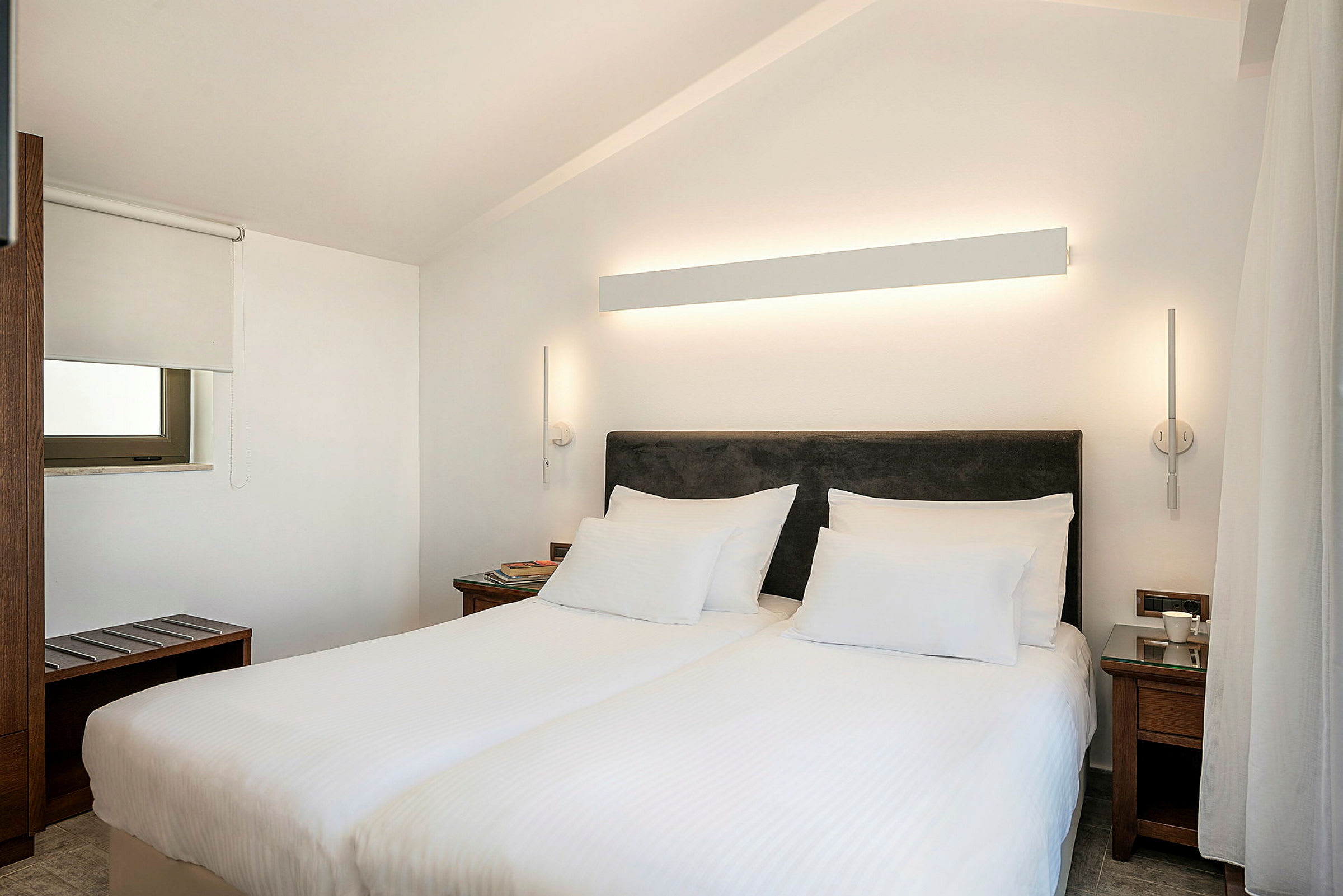 Hotellihuone, jossa on kaksi erillistä sänkyä, valkoinen seinä ja moderni valaistus. (Tekoälyn luoma teksti)