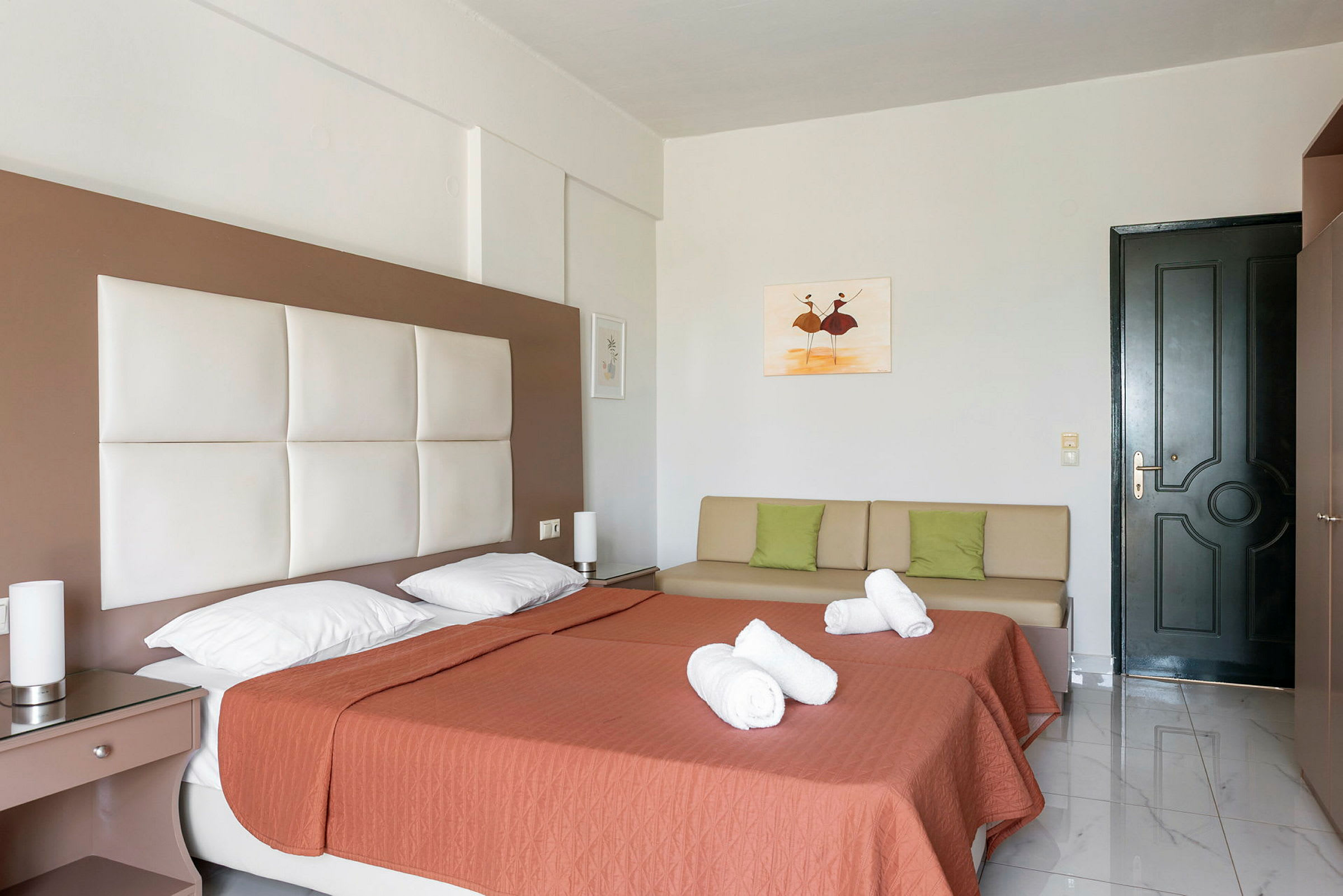 Hotellihuone, jossa kaksi yhden hengen vuodetta, tyynyliinat, sohva ja ovi. (Tekoälyn luoma teksti)