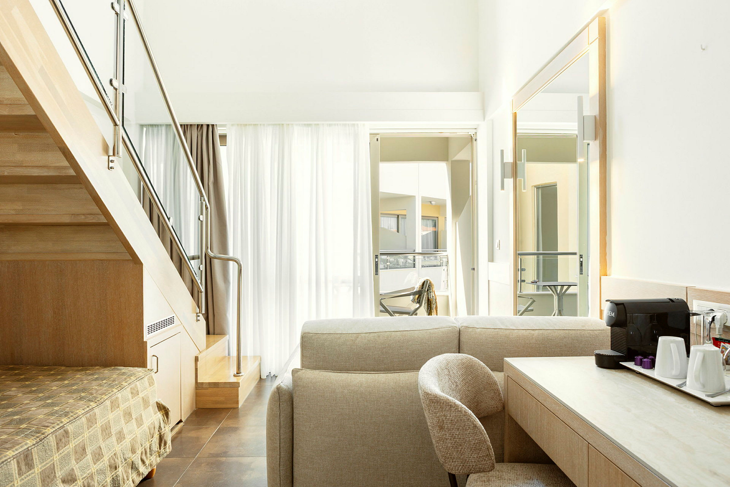 Sisäkuva modernista hotellihuoneesta, jossa on portaat, istuinryhmä ja kirjoituspöytä kahvinkeittimellä. (Tekoälyn luoma teksti)