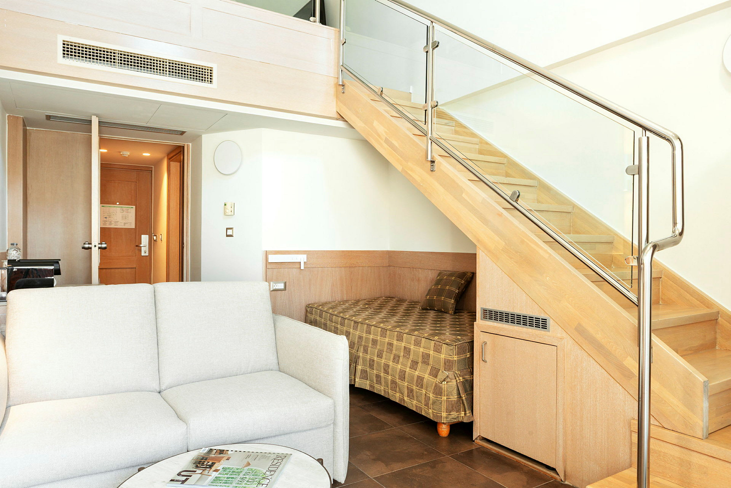 Hotellihuone, jossa on sohva, pöytä ja kerrossänky portaiden alla. (Tekoälyn luoma teksti)