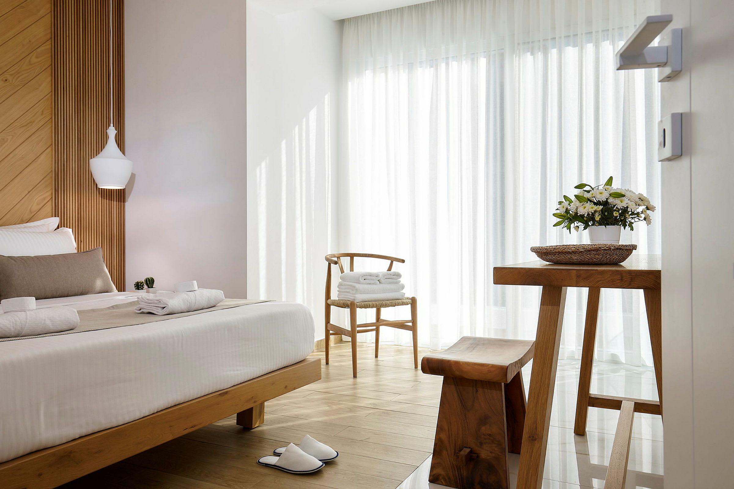 Valoisa ja ilmava hotellihuone puuyksityiskohdilla, pedattu sänky, kukkaruukku pöydällä ja pari valkoisia tohveleita lattialla. (Tekoälyn luoma teksti)