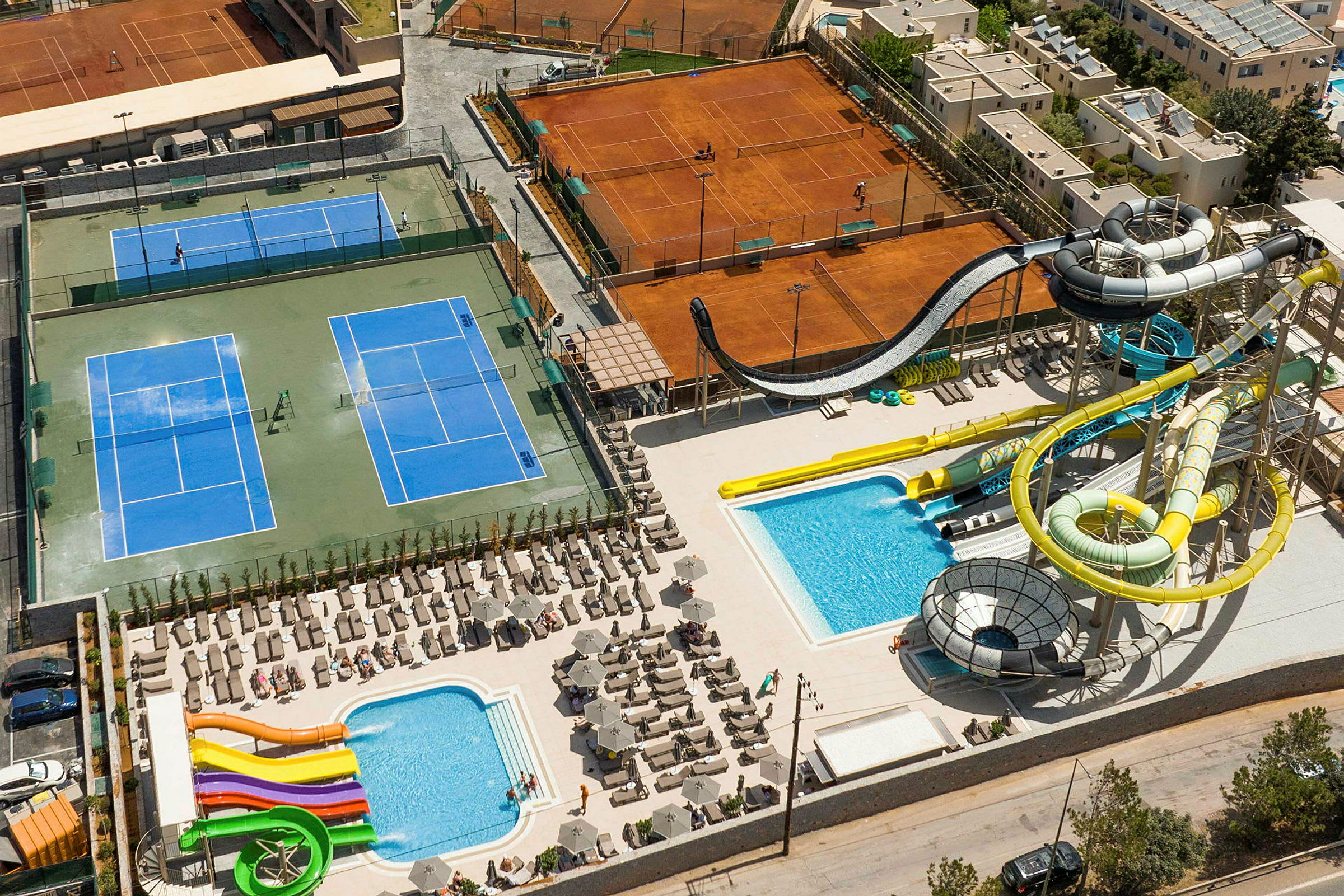Kuva tennis- ja uima-allasalueista vesiliukumäkineen. (Tekoälyn luoma teksti)