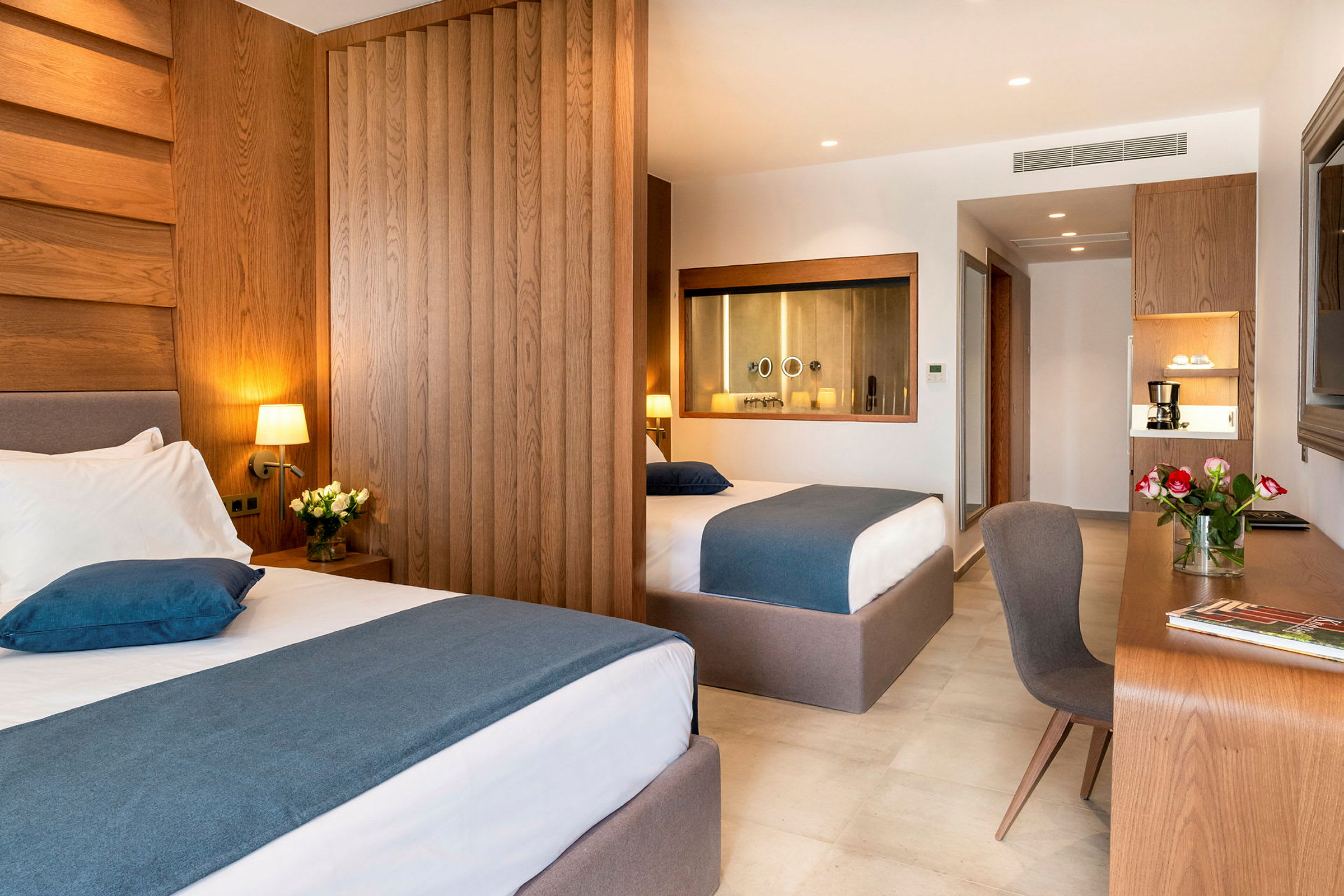 Hotellihuone, jossa on kaksi sänkyä, työpöytä ja kukkia. (Tekoälyn luoma teksti)