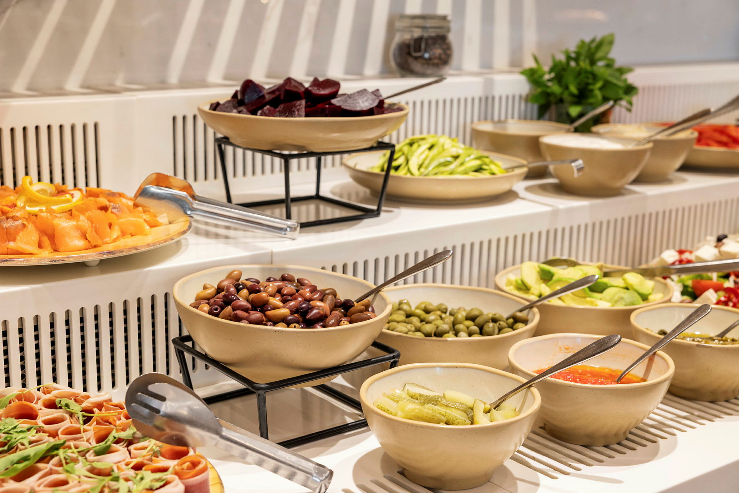 Buffet, jossa on erilaisia kulhoja täynnä salaatteja, oliiveja ja muita ruokia. (Tekoälyn luoma teksti)