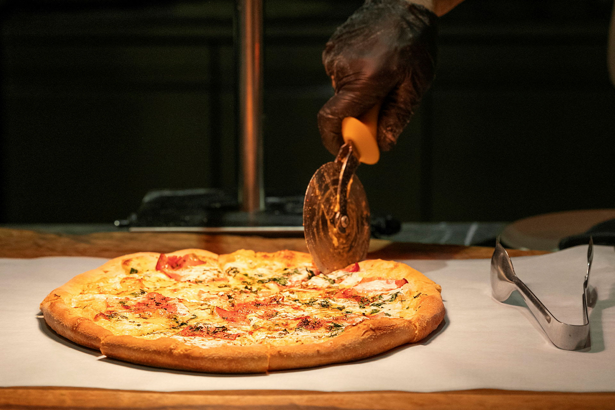 Pizza leikataan leivinpaperilla pizzaleikkurilla, jota pitää kädessä mustakäsinemies. (Tekoälyn luoma teksti)