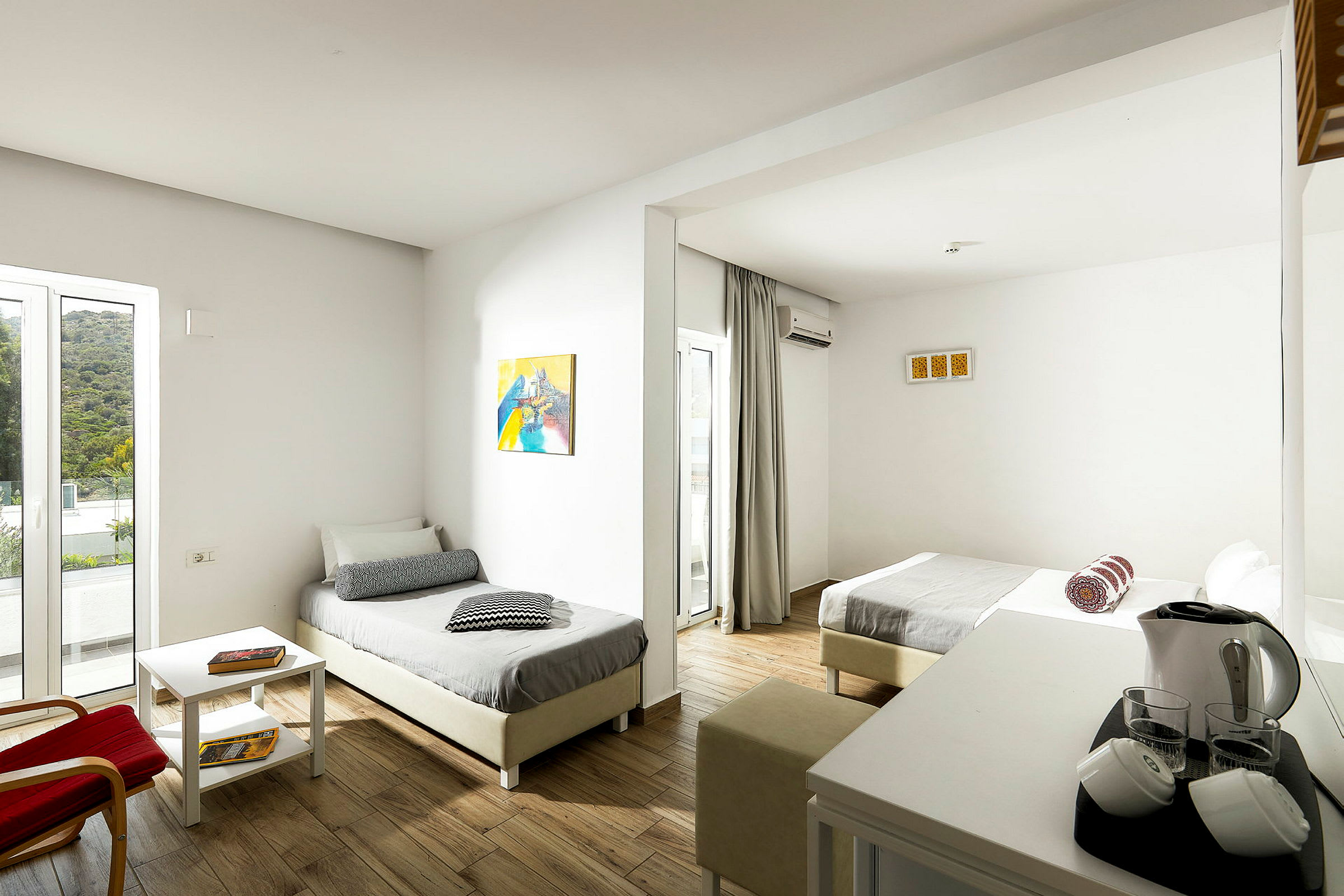 Kuva hotellihuoneesta, jossa kaksi erillistä vuodetta, vaaleat seinät ja huonekalut sekä pöytä elektronisilla palveluilla. (Tekoälyn luoma teksti)