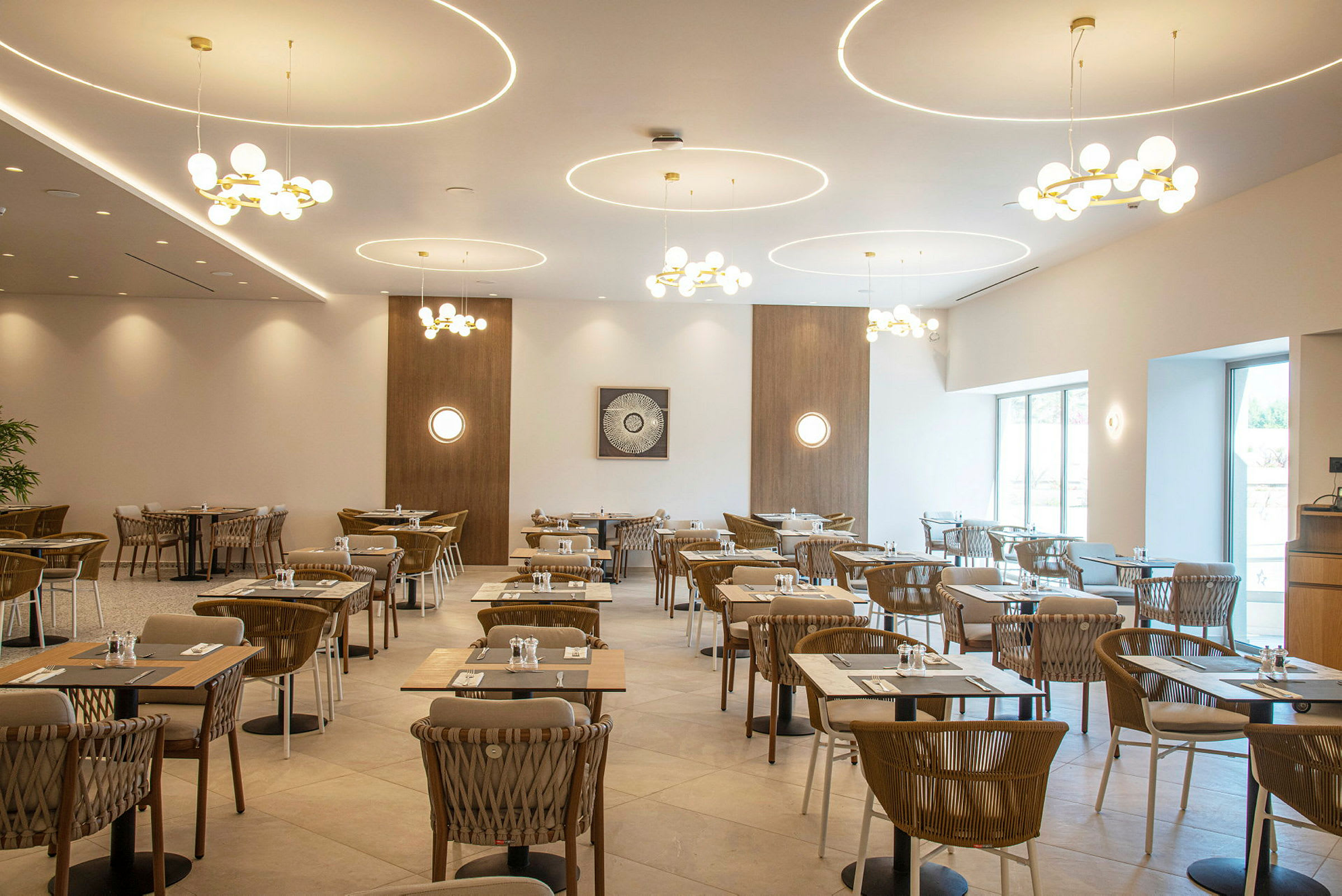 Ravintola, jossa on modernit kalusteet ja sisustus, katettuja pöytiä ja tuoleja. Kattokruunut roikkuvat katosta. (Tekoälyn luoma teksti)