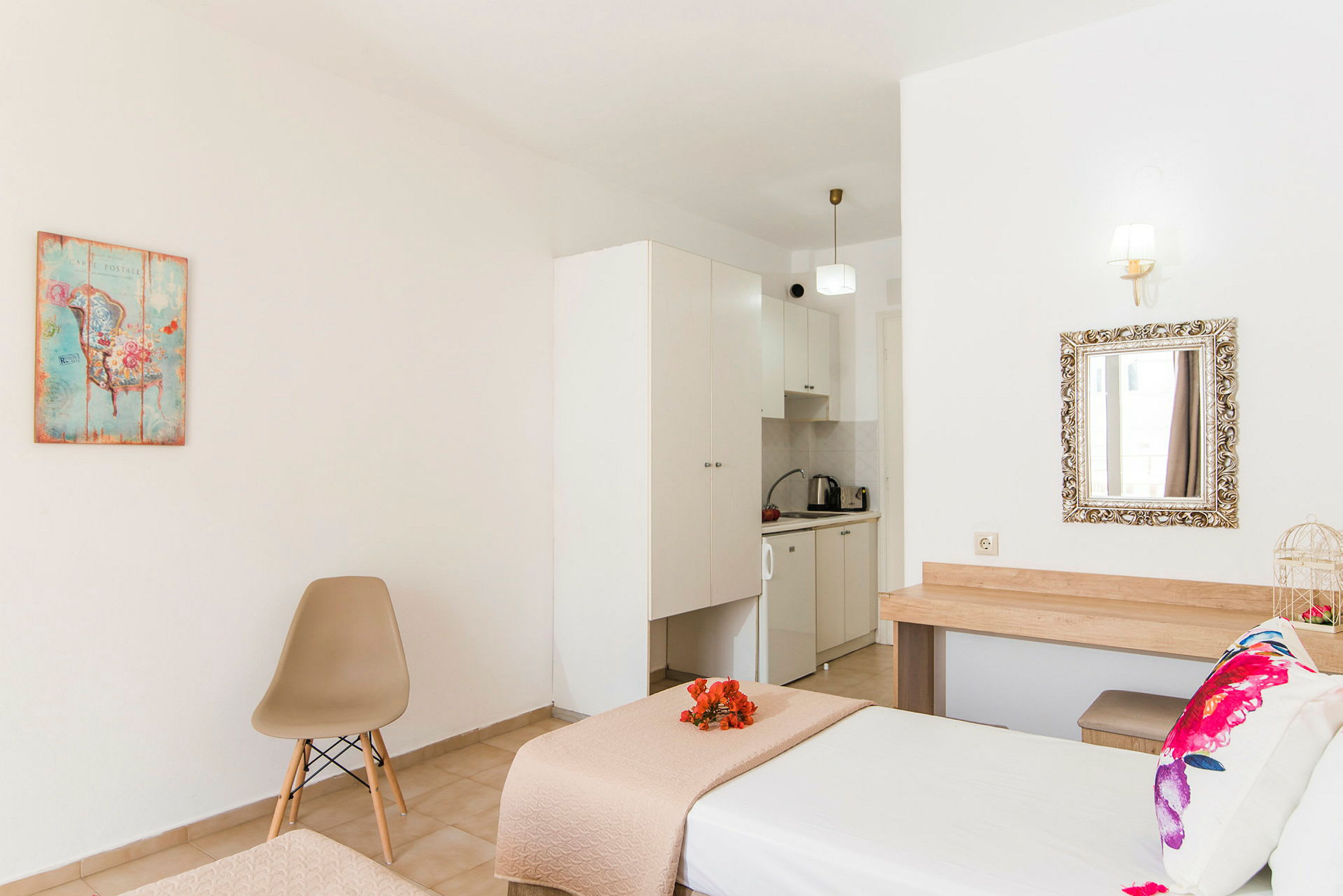 Hotellihuone, jossa on sänky, tuoli, koristeellinen taulu ja pieni keittiötila. (Tekoälyn luoma teksti)