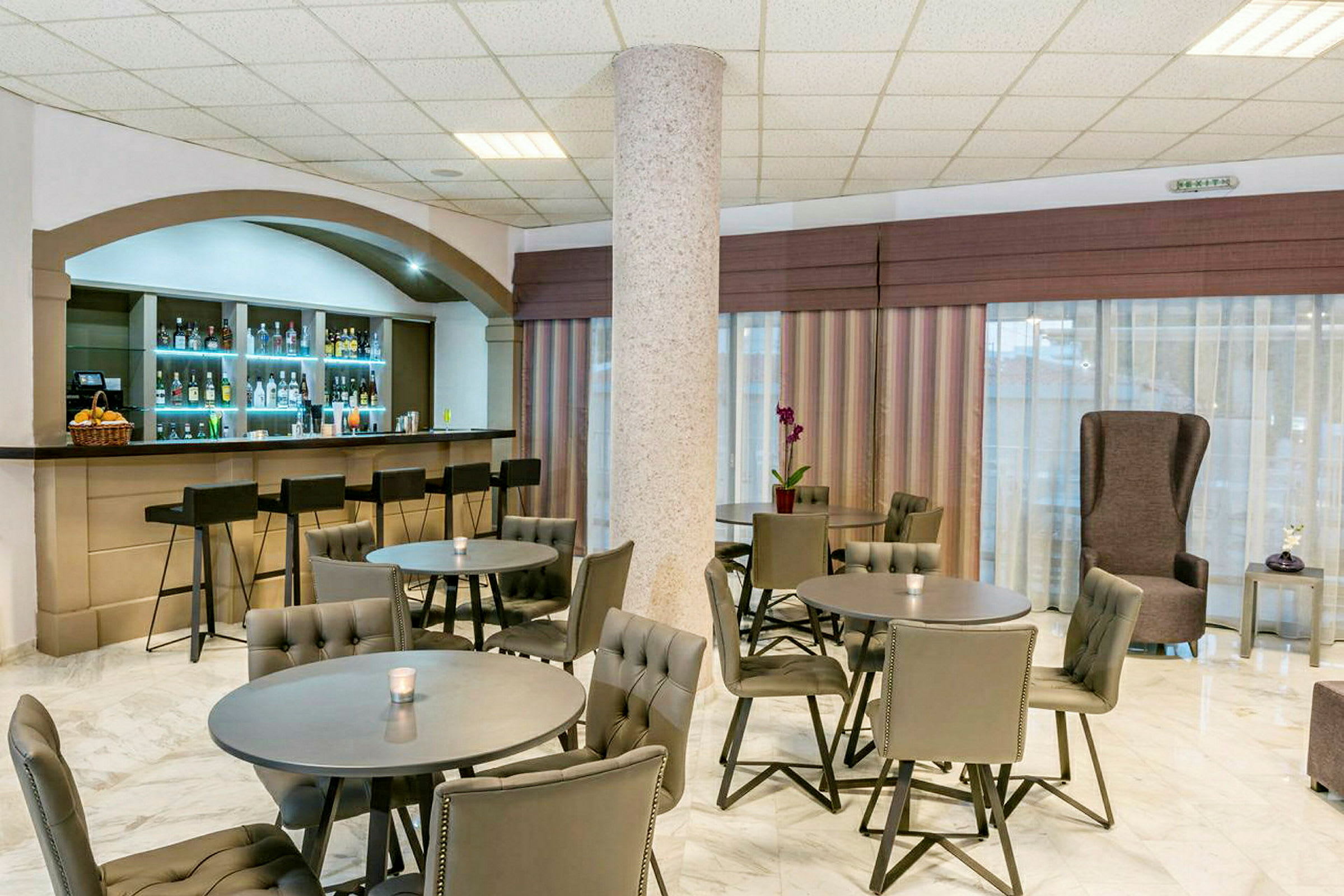 Kuva hotellibaarista, jossa on useita pöytiä ja tuoleja sekä baaritiski ja baarijakkaroita. (Tekoälyn luoma teksti)